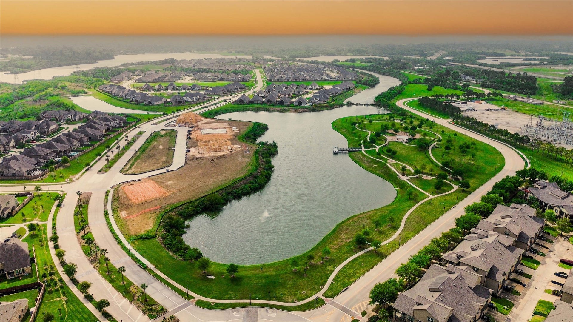 This aerial photo showcases a serene residential neighborhood featuring a winding lake, surrounded by well-maintained homes and lush greenery. Curved roads and walking paths enhance the picturesque setting, ideal for families seeking a tranquil and scenic living environment.