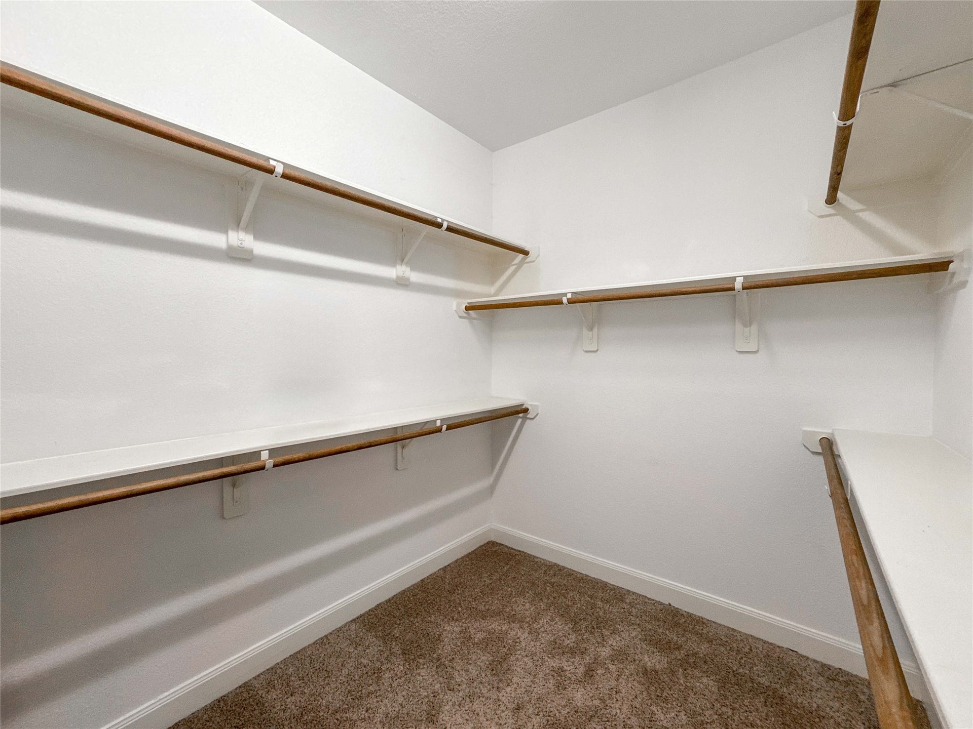 This photo shows a spacious walk-in closet with multiple wooden hanging rods and white shelves, perfect for organizing clothing and accessories. The carpeted floor adds warmth and comfort.
