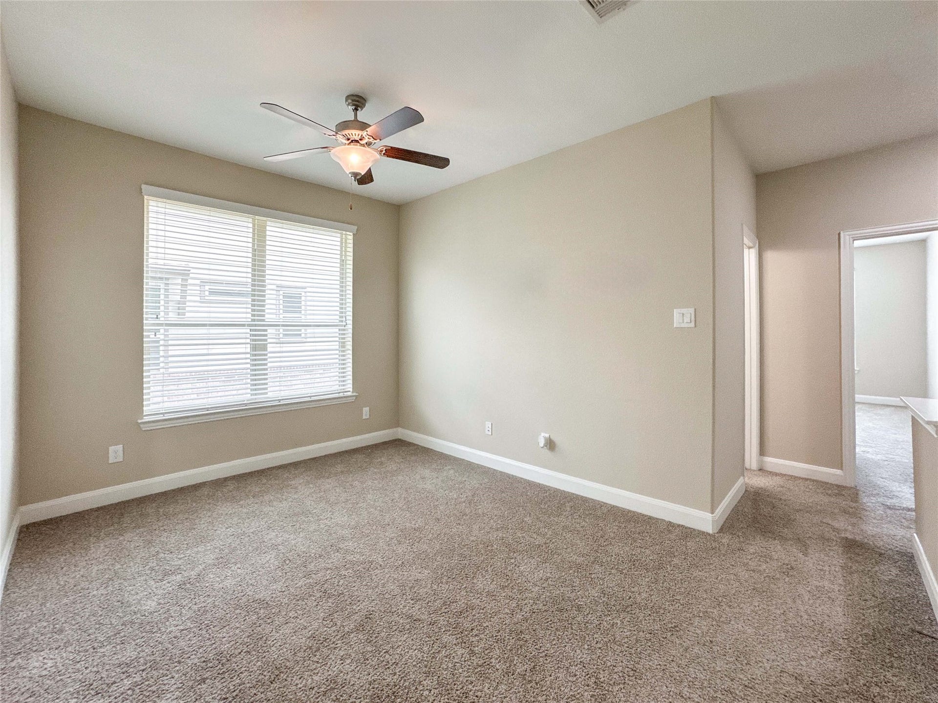 Enjoy this bright, spacious game room located on the second floor, with neutral walls and carpeted flooring. It features a ceiling fan and a large window offering natural light. There is an adjoining hallway leading to the secondary bedrooms.