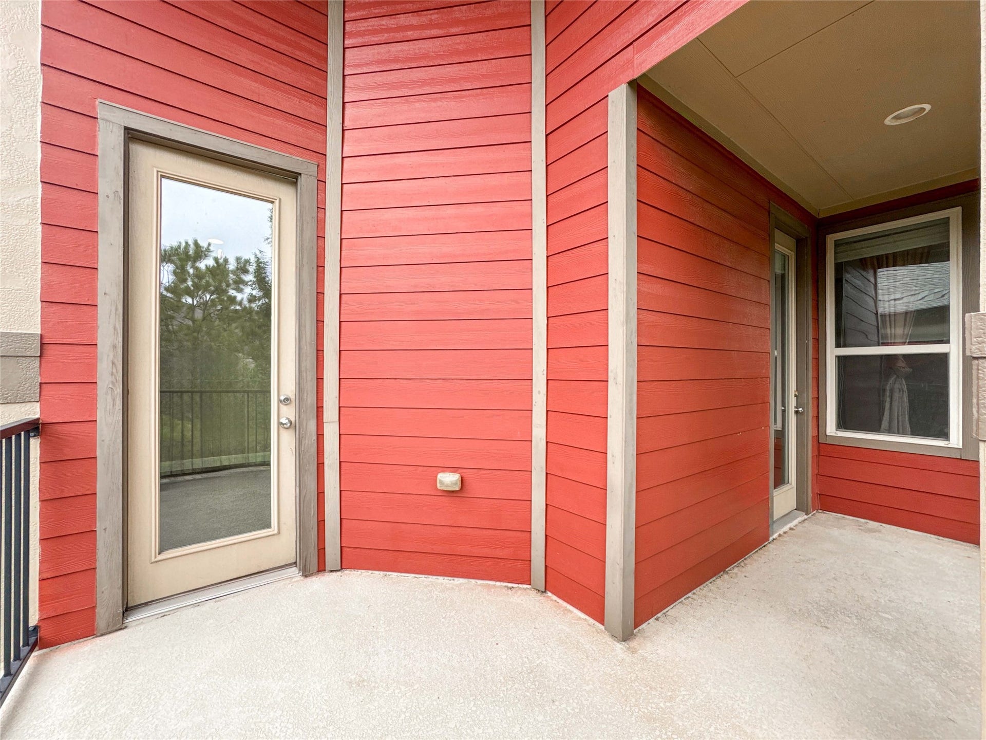 This photo showcases a vibrant red exterior with modern wood siding and two glass doors leading to a balcony or patio. The space is covered, providing shelter and a cozy outdoor area.