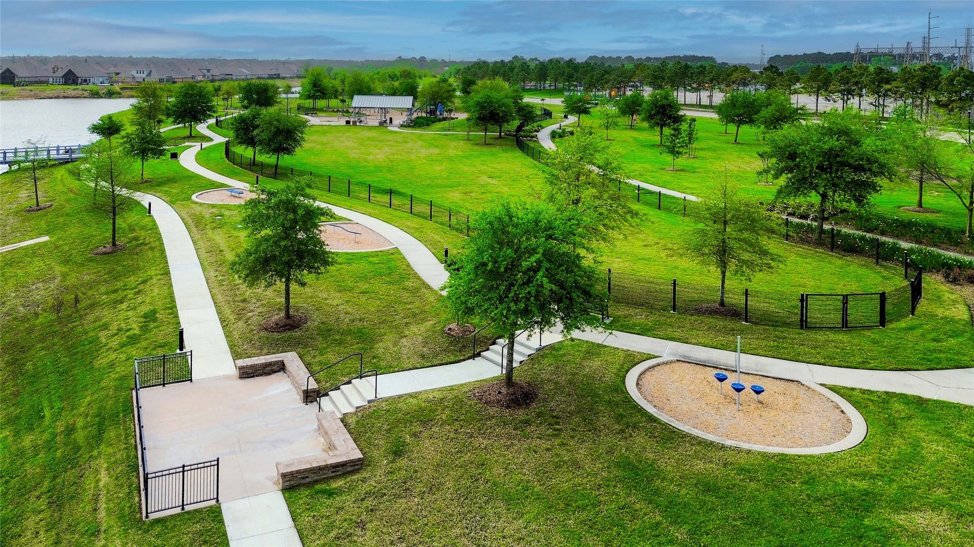 This photo showcases a spacious, well-maintained park with winding pathways, lush green lawns, and scattered trees. There's a playground area and a scenic view of a nearby water body, making it ideal for families and outdoor activities.