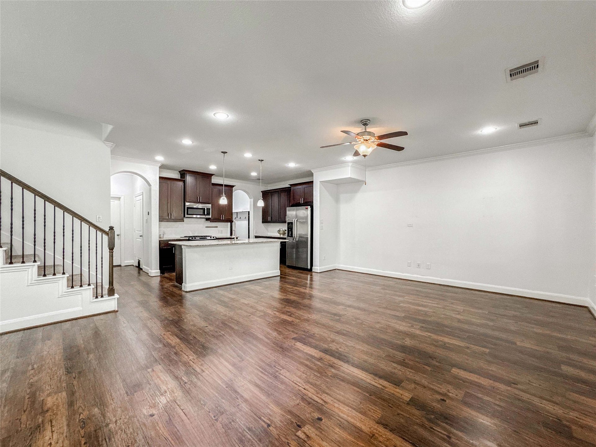 This spacious open-concept room features luxury vinyl floors and a granite kitchen with dark cabinetry, stainless steel appliances, and a central island. Adjacent is a living area with ceiling fan and ample natural light, perfect for entertaining.