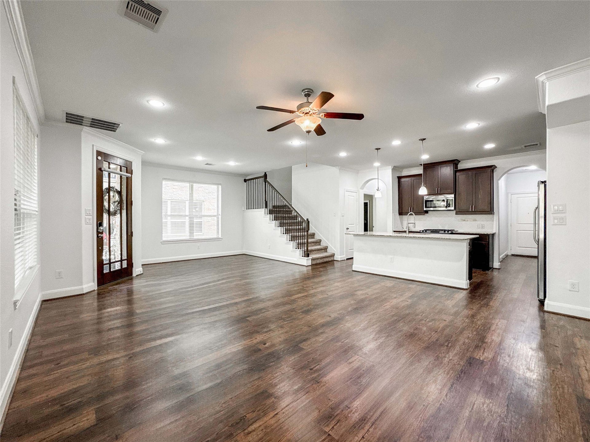 Spacious open-concept living area with luxury vinyl floors, modern kitchen featuring an island and dark cabinetry, ceiling fan, and ample natural light. Includes a staircase leading upstairs, a cozy breakfast nook and welcoming front entry.