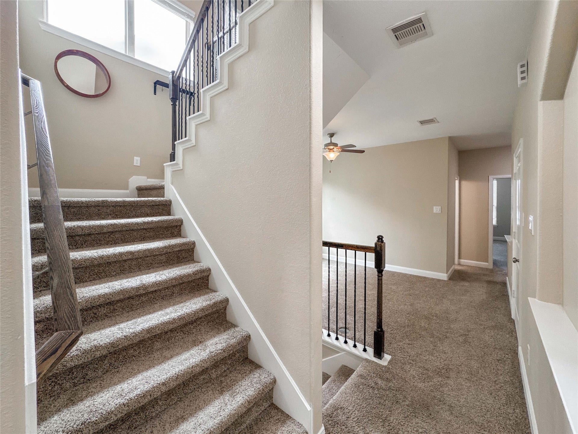 This photo showcases a bright, carpeted staircase with wooden handrails leading to a landing area. The space features neutral walls and a ceiling fan, providing a welcoming and cozy atmosphere.