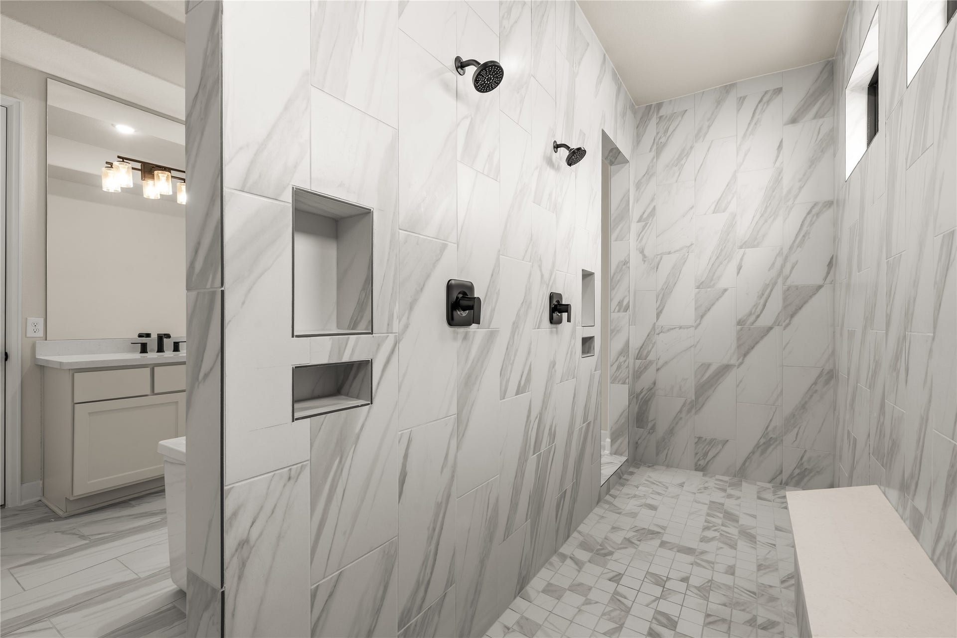 9607 Maple Wood Drive, Missouri City, TX 77459 Luxurious walk-in shower featuring elegant marble, dual showerheads, built-in niches, and a sleek bench for ultimate relaxation.