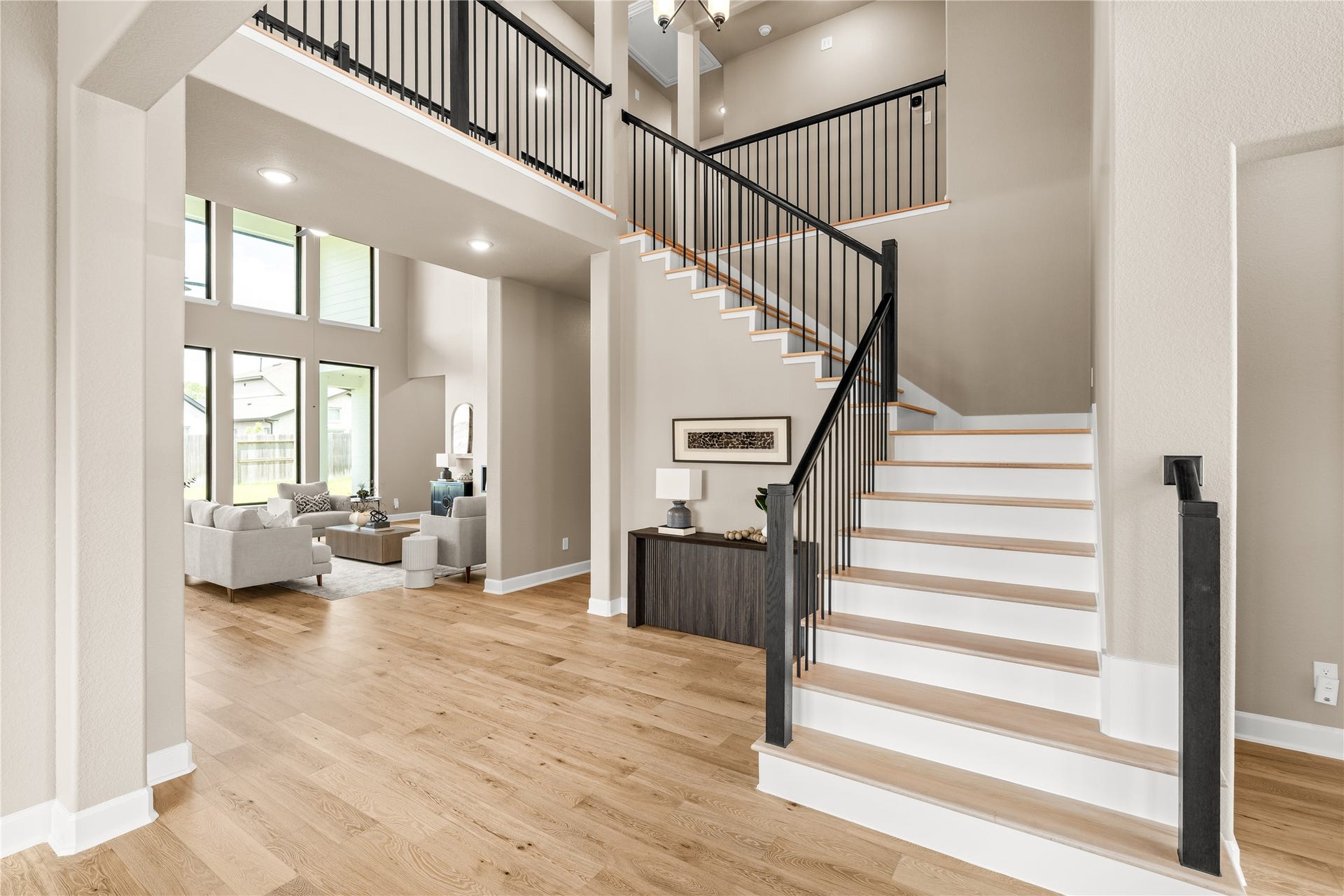 9607 Maple Wood Drive, Missouri City, TX 77459 A grand open-concept living space with soaring ceilings, abundant natural light from large windows, and elegant hardwood floors, complemented by a modern staircase leading to the upper level. *Virtually Staged*