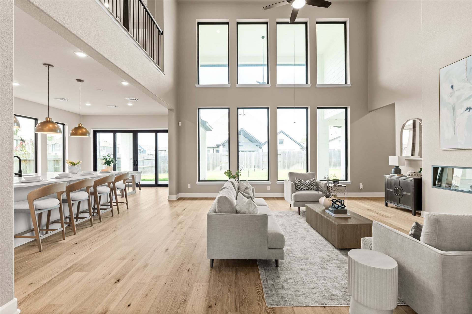 9607 Maple Wood Drive, Missouri City, TX 77459 Expansive living area with soaring ceilings and abundant natural light from floor-to-ceiling windows, seamlessly connecting to a modern kitchen with sleek island and elegant pendant lighting. *Virtually Staged*