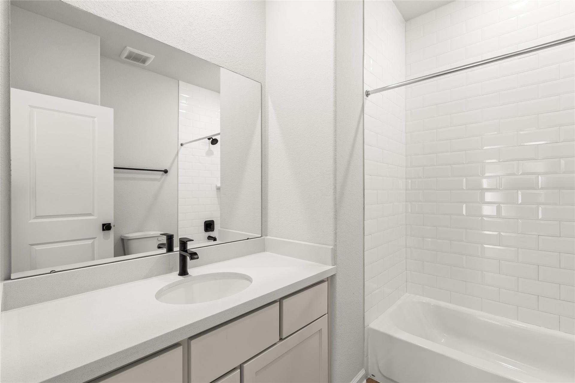 9607 Maple Wood Drive, Missouri City, TX 77459 Modern bathroom showcasing a sleek vanity with a black faucet, elongated mirror, and a pristine white-tiled bathtub.