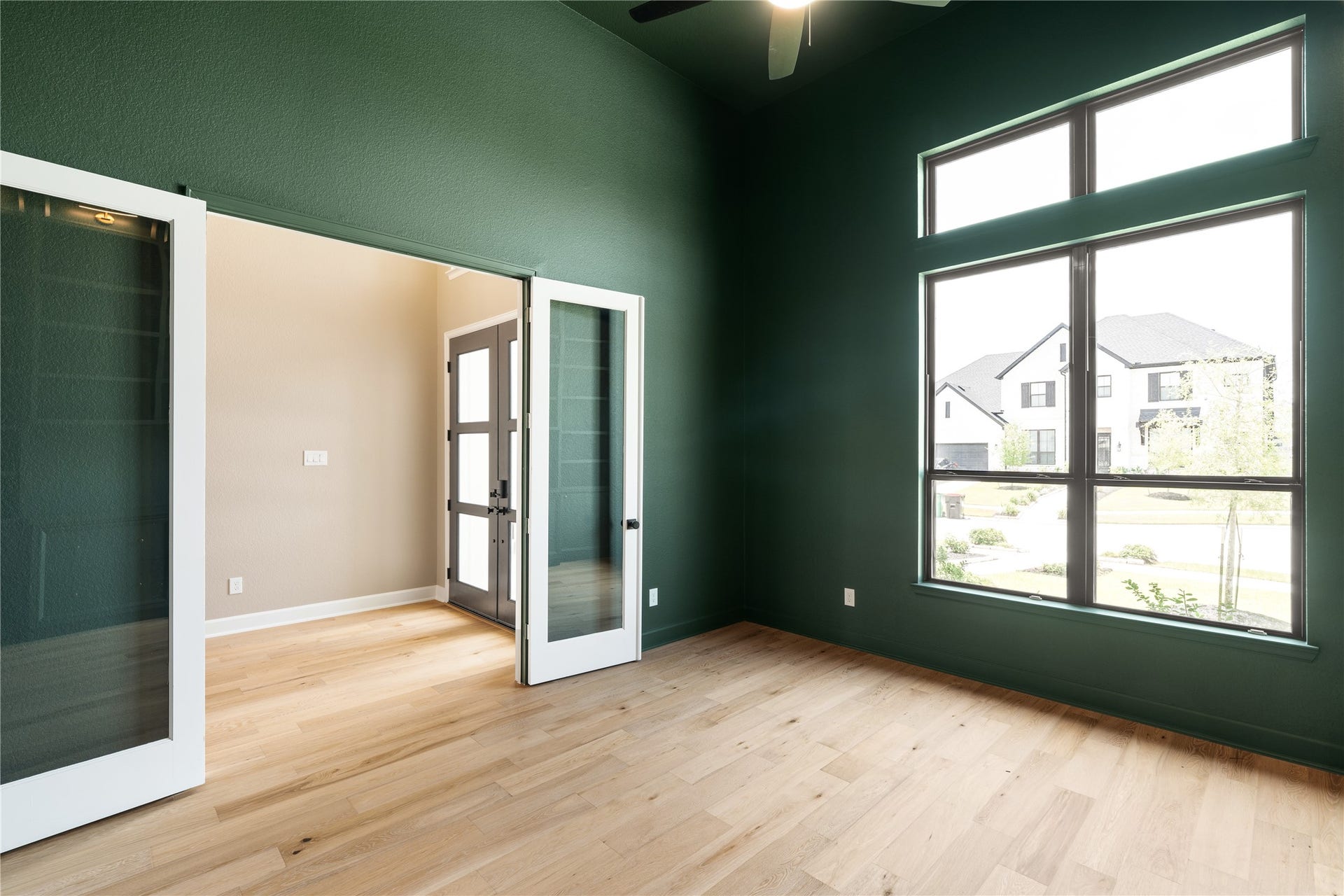 9607 Maple Wood Drive, Missouri City, TX 77459 A spacious study with elegant green walls features large windows for abundant natural light and sleek glass double doors, complemented by light wood flooring for a modern and inviting atmosphere.