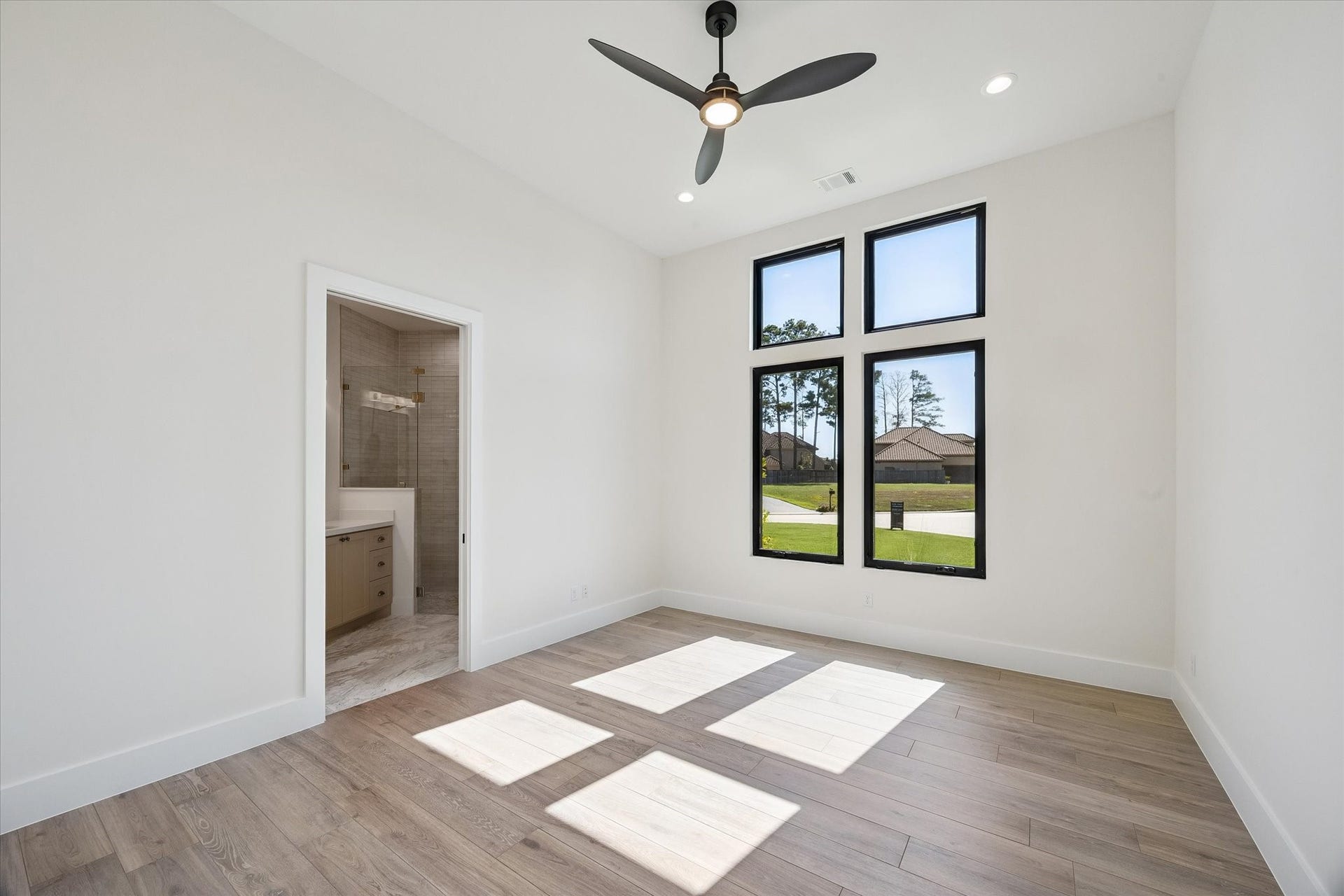 65 Shadow Creek Ridge Drive, Spring, TX 77389 Sunlit downstairs secondary bedroom with tall black-framed windows, wood-style floors, and a private ensuite bath.