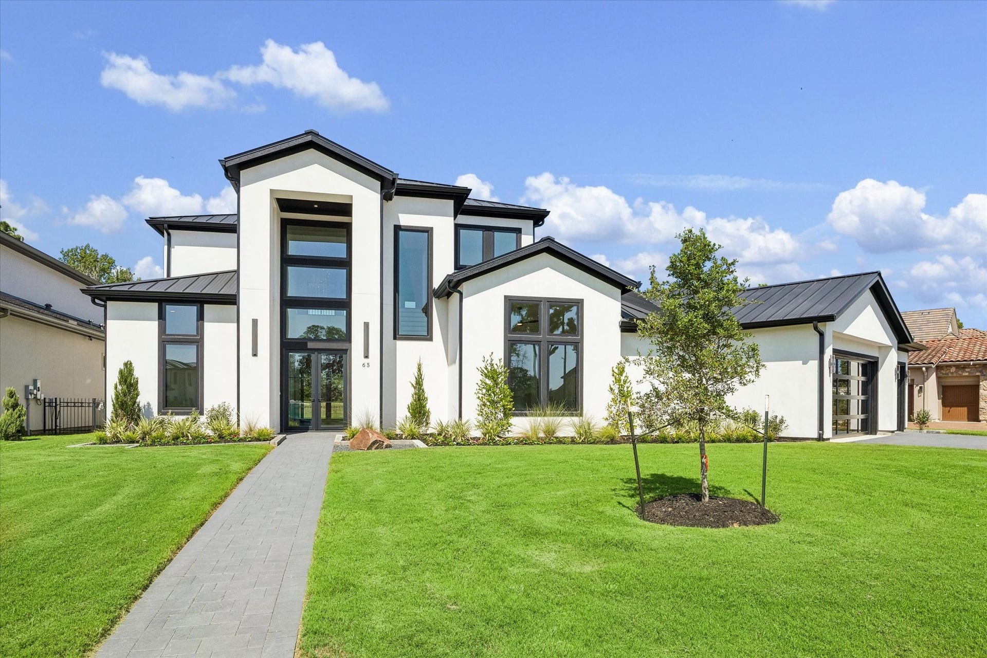 65 Shadow Creek Ridge Drive, Spring, TX 77389 Striking modern facade with standing-seam metal roof, oversized windows, and crisp landscaping on a wide lawn.