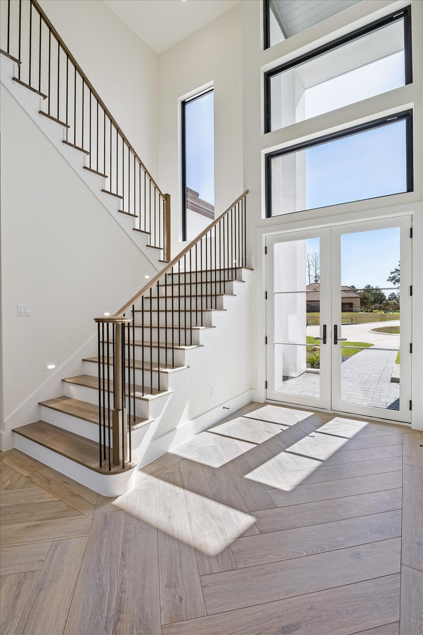 65 Shadow Creek Ridge Drive, Spring, TX 77389 Sun-filled foyer with soaring ceilings, dramatic windows, and a modern staircase over wide-plank flooring.