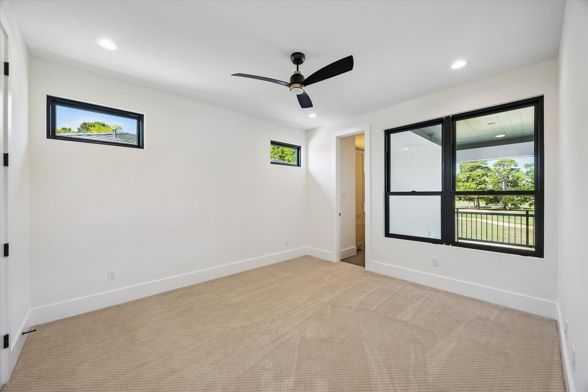 65 Shadow Creek Ridge Drive, Spring, TX 77389 Sunlit upstairs secondary bedroom with modern ceiling fan, plush carpet, and oversized windows framing peaceful golf course views and ensuite.