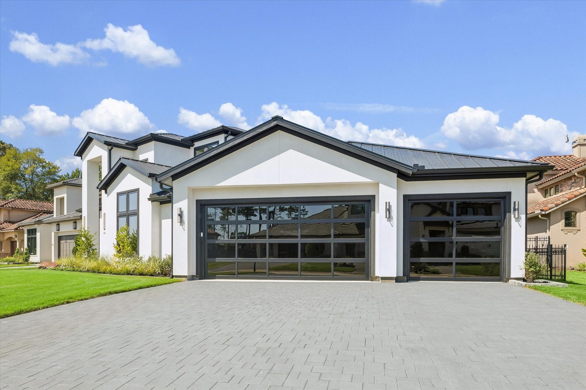 65 Shadow Creek Ridge Drive, Spring, TX 77389 The wide paver driveway leads to an oversized multi-bay garage with contemporary glass-panel doors, plus clean-lined wall-mounted exterior lighting for a polished finish day or night.