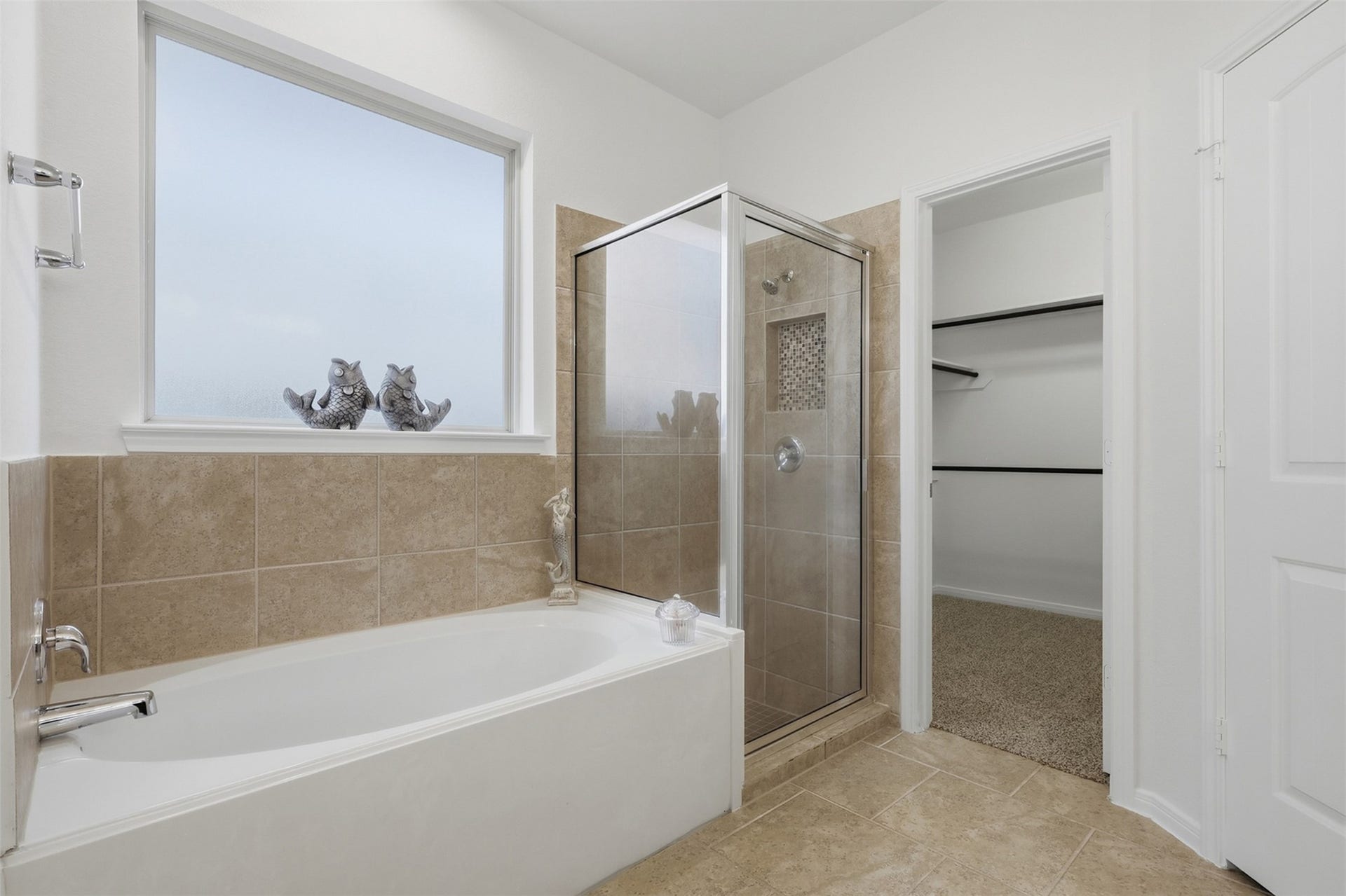 11723 Giovanni Lane, Richmond, TX 77406 Relax, Refresh & Enjoy! This inviting primary bath showcases a beautiful soaking tub positioned beneath a large window, a separate glass-enclosed shower, and a spacious walk-in closet just beyond. The warm tile finishes and abundant natural light give the room a bright, comfortable feel. A wonderful private retreat within this lovely primary suite!