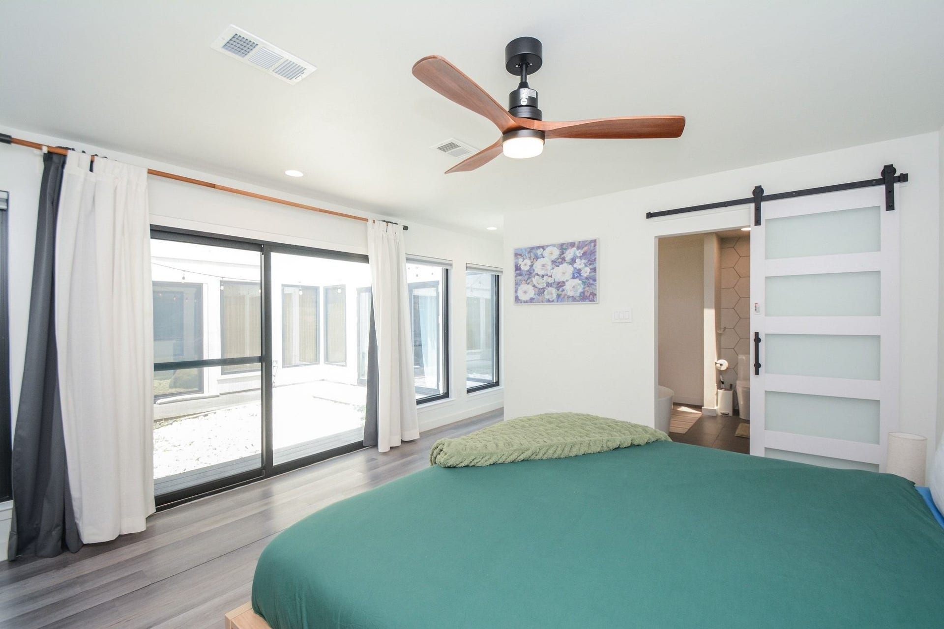 Spacious primary bedroom with updated flooring, ceiling fan, and large windows overlooking the courtyard.