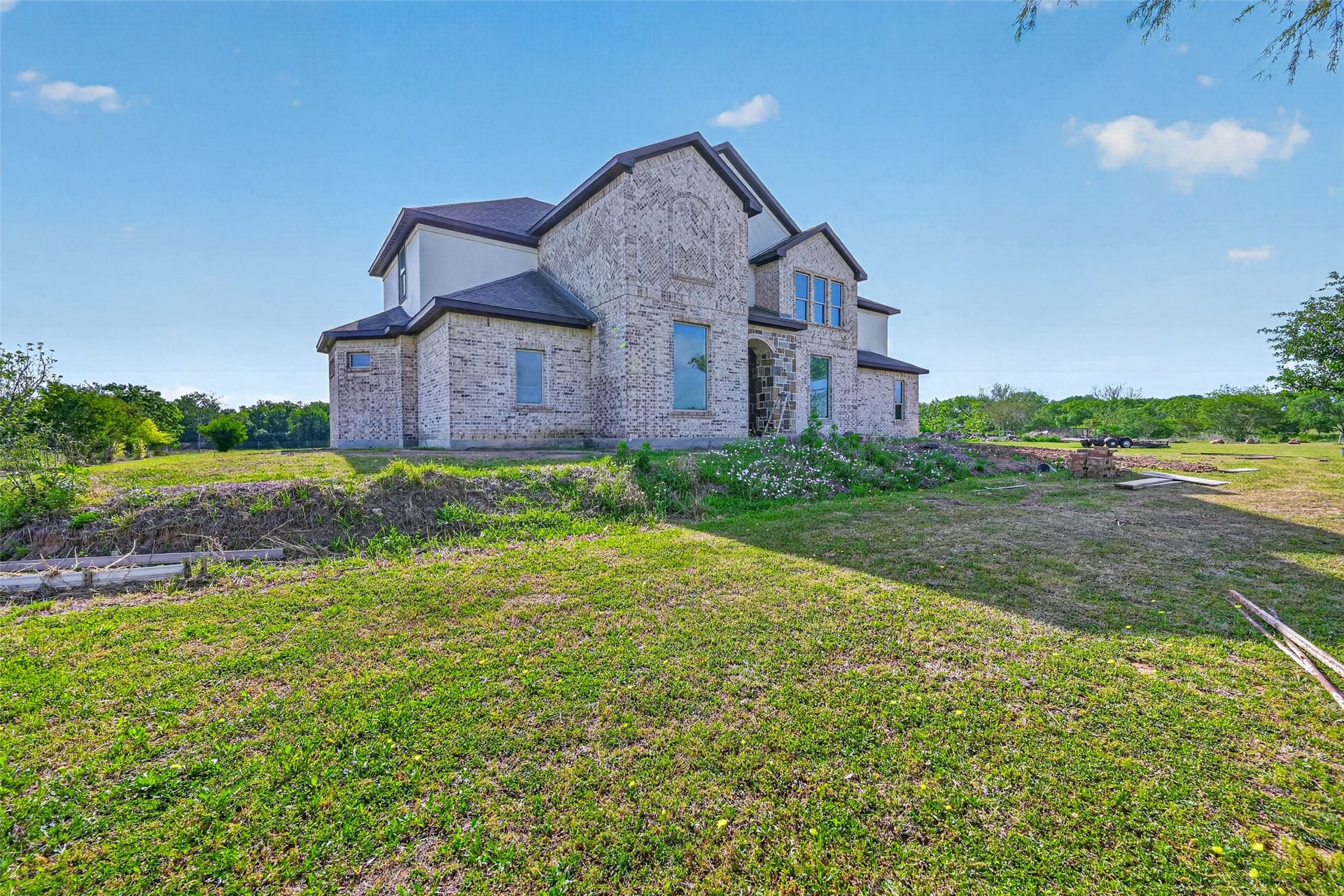 8023 Pool Hill Road, Fulshear, TX 77441 Angled front exterior view of Property 1 unfinished residence showcasing the scale of the structure, surrounding open space, and existing lawn.