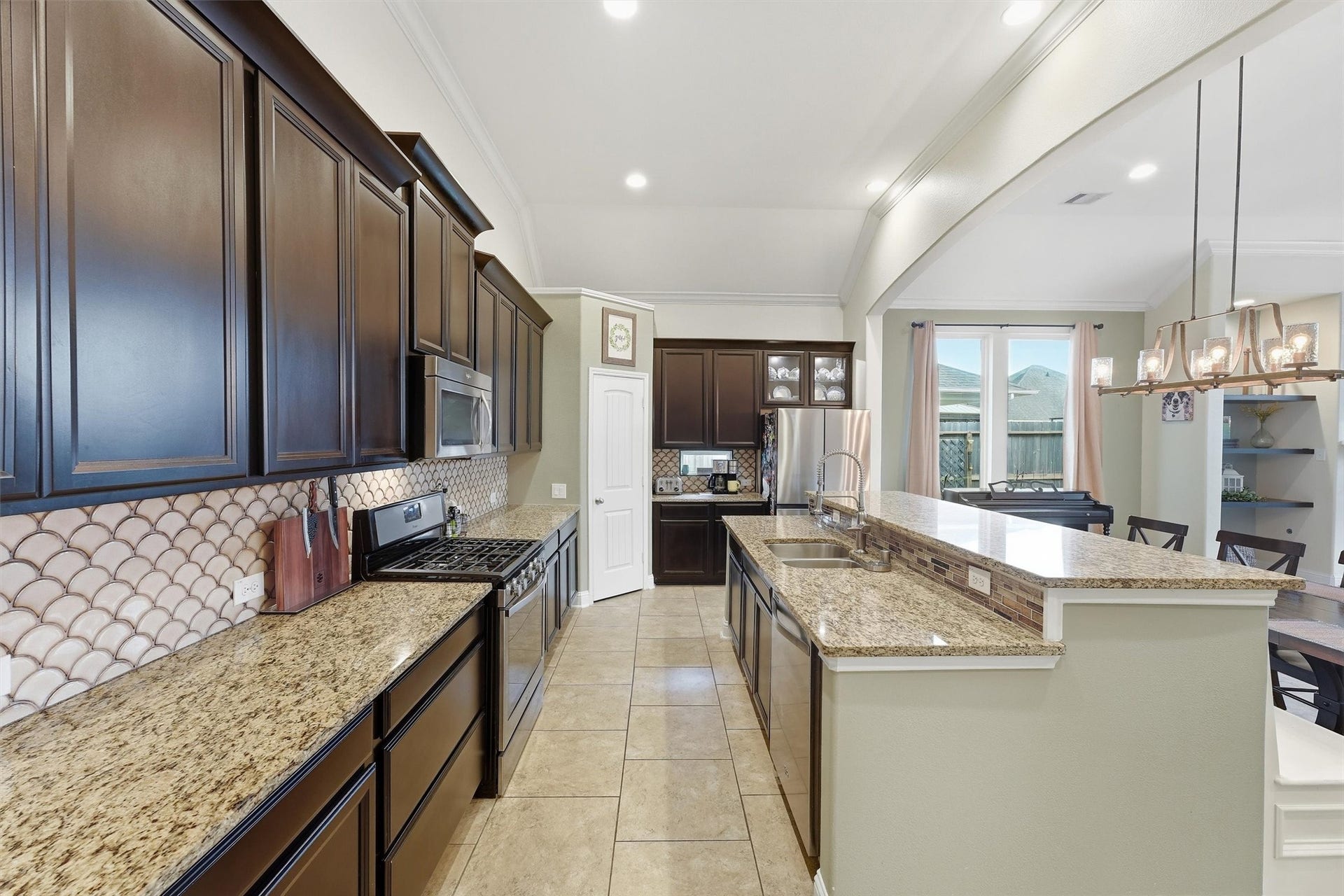 1413 Silver Rings Court, Pearland, TX 77581 Elegant kitchen featuring dark wood cabinetry, granite countertops, and a stylish tile backsplash. The open layout flows into a bright dining area with modern lighting.