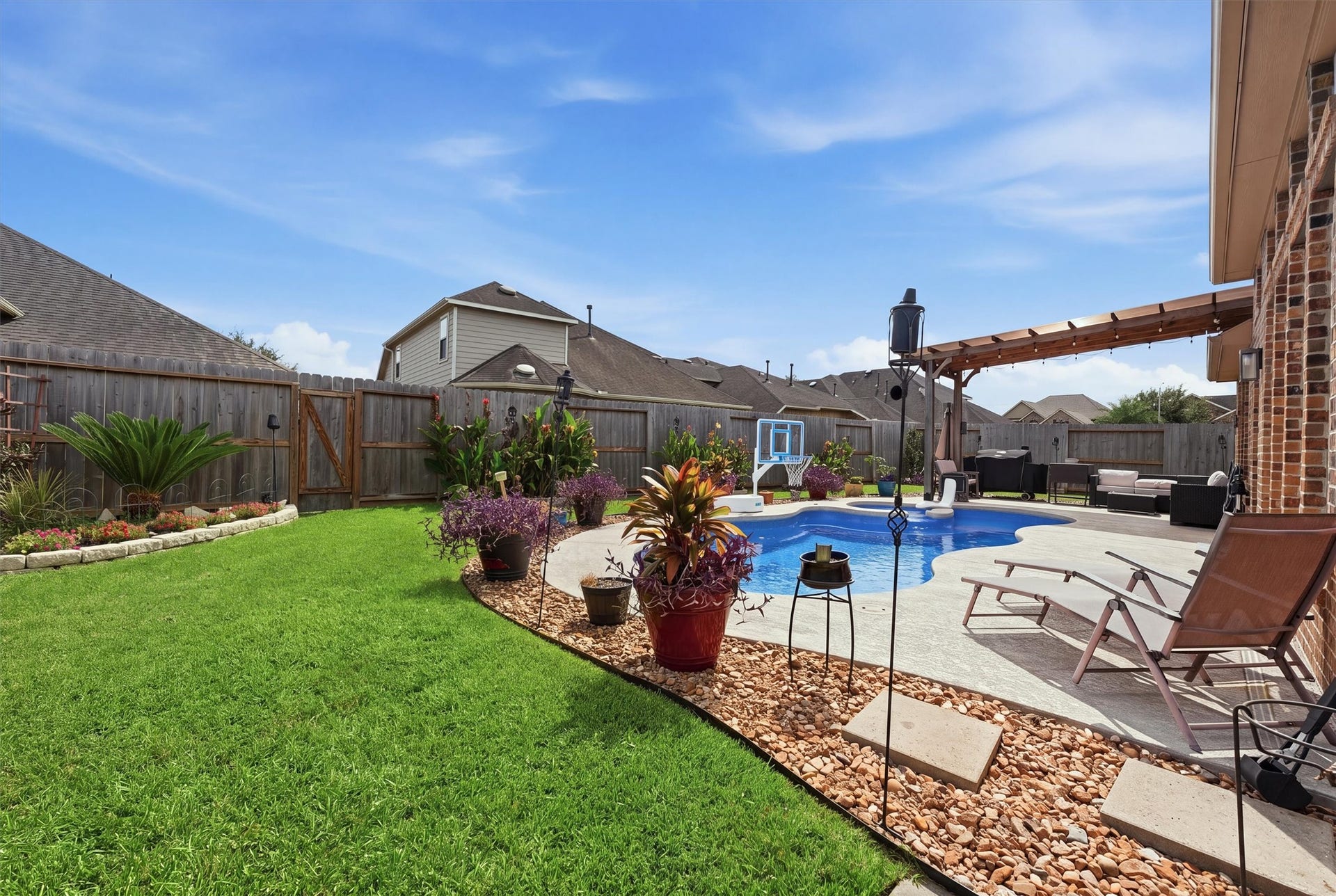 1413 Silver Rings Court, Pearland, TX 77581 Charming backyard oasis featuring a sparkling pool, lush green lawn, and a cozy pergola-covered seating area perfect for relaxation and entertaining.