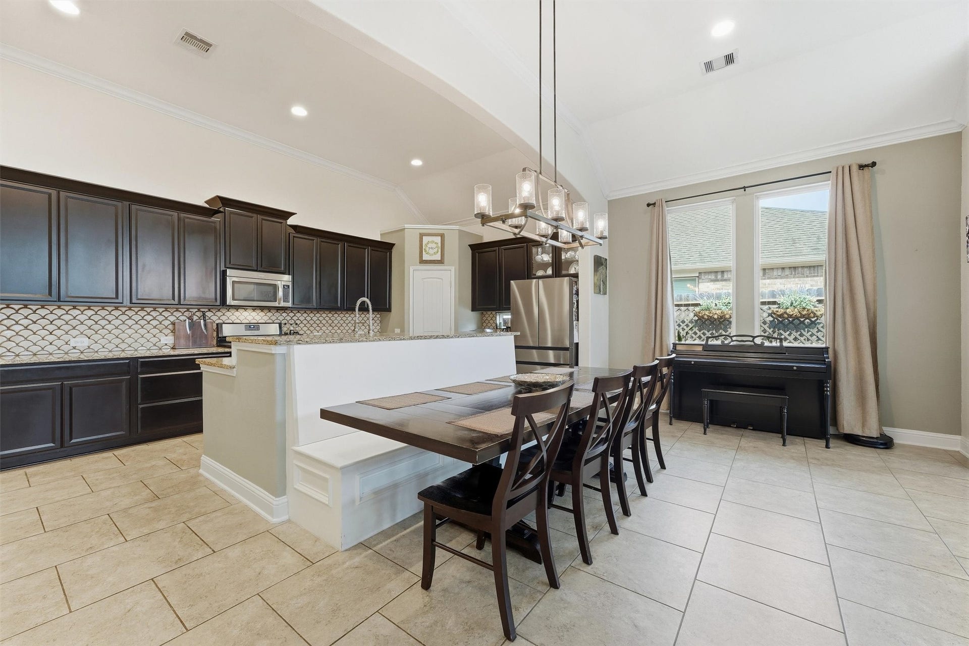 1413 Silver Rings Court, Pearland, TX 77581 Spacious kitchen and dining area featuring modern dark cabinetry, stainless steel appliances, and a stylish tile backsplash. Built-in dining seating with storage was added.