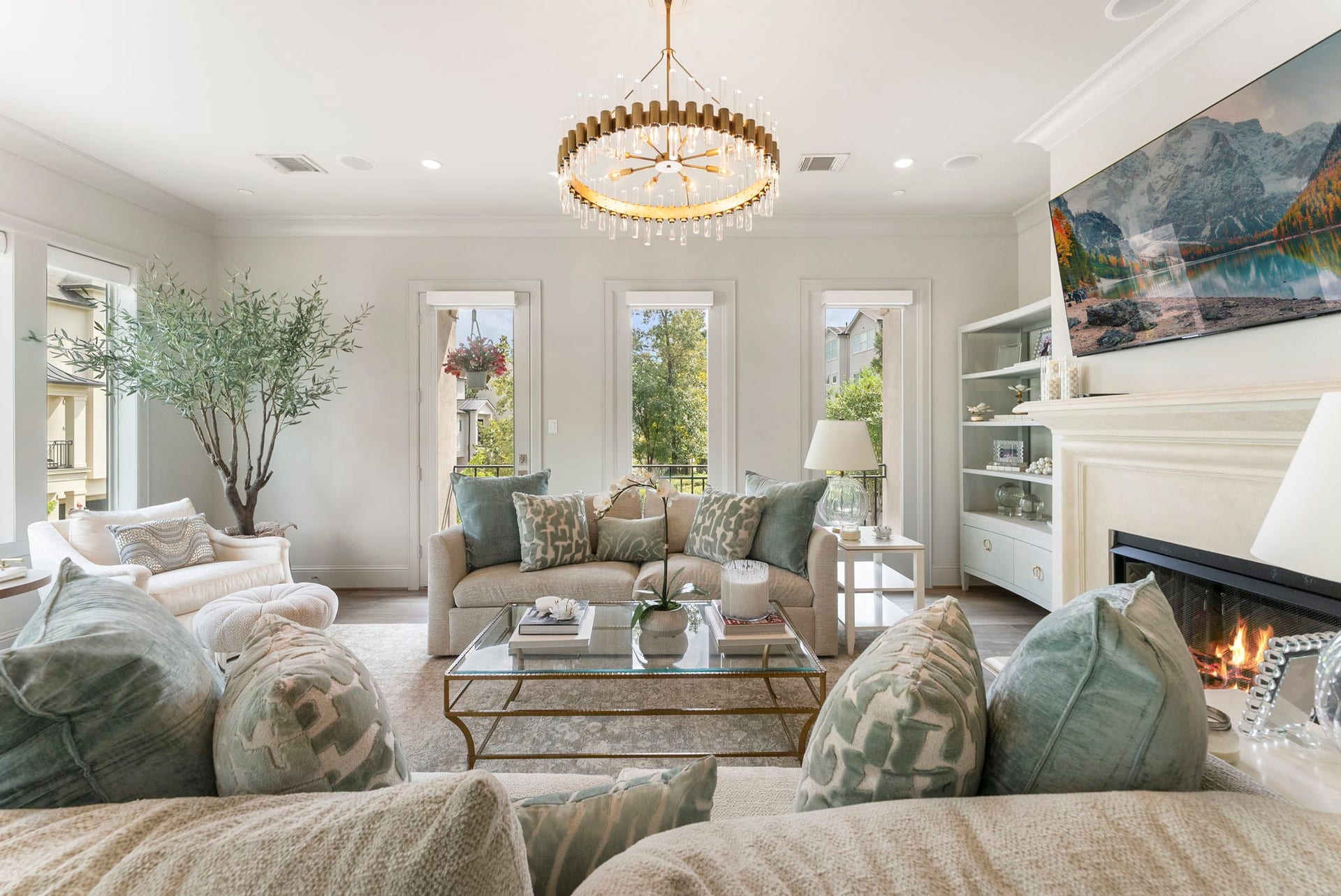 10 Nautical Terrace Way, The Woodlands, TX 77380 Light-filled living room with gas-log fireplace, designer chandelier and private balcony framed by lush treetop views, a peaceful everyday gathering space.