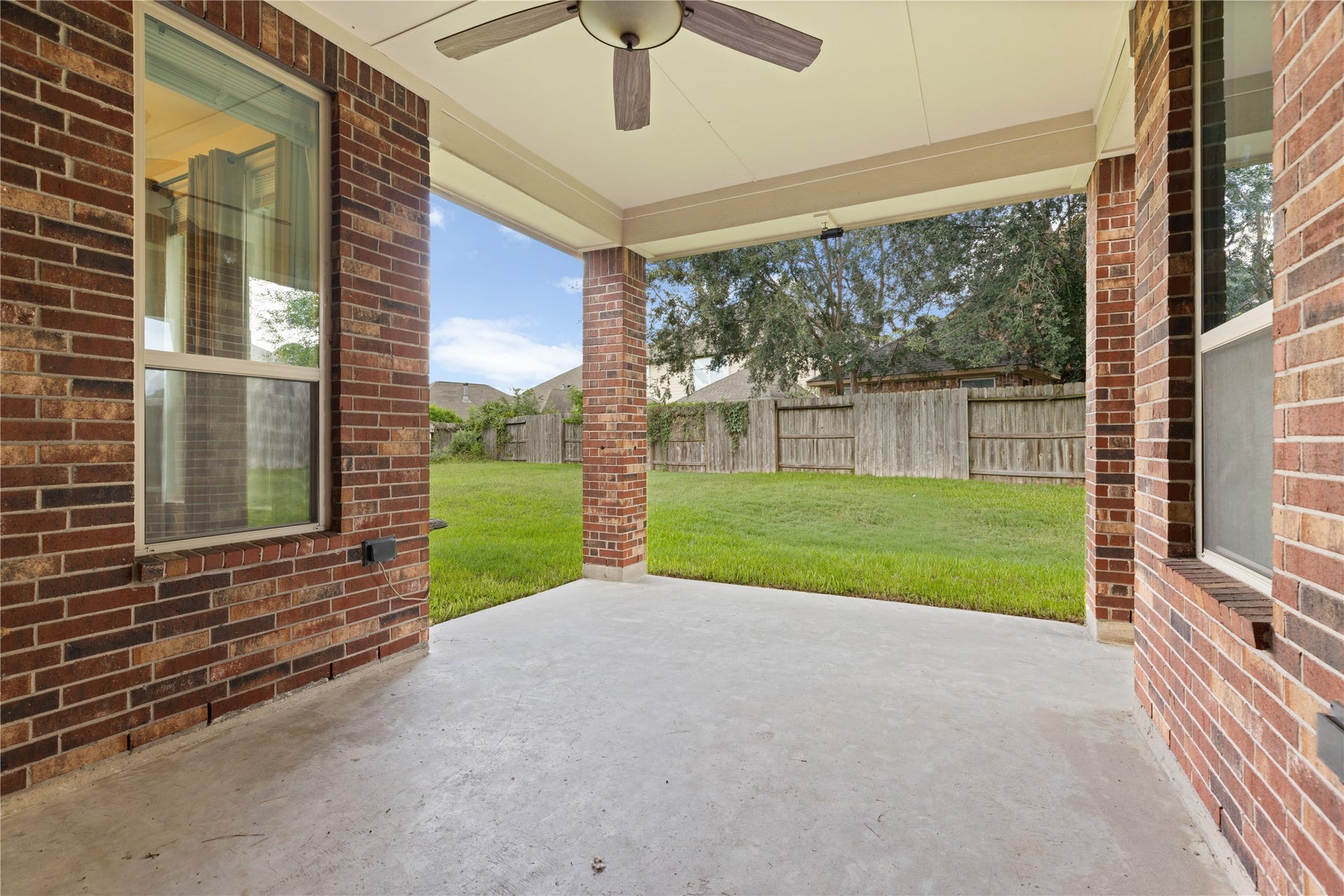 20507 Emery Manor Lane, Porter, TX 77365 Charming covered patio with brick accents and ceiling fan, overlooking a spacious backyard perfect for relaxation and outdoor gatherings.