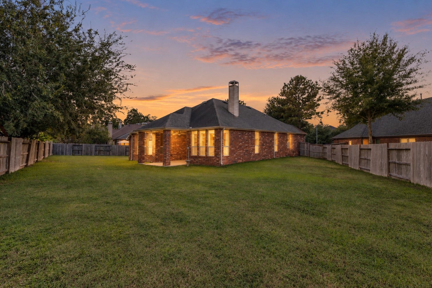 20507 Emery Manor Lane, Porter, TX 77365 Charming brick home with a spacious, fenced backyard perfect for outdoor activities and entertaining, set against a picturesque sunset backdrop.