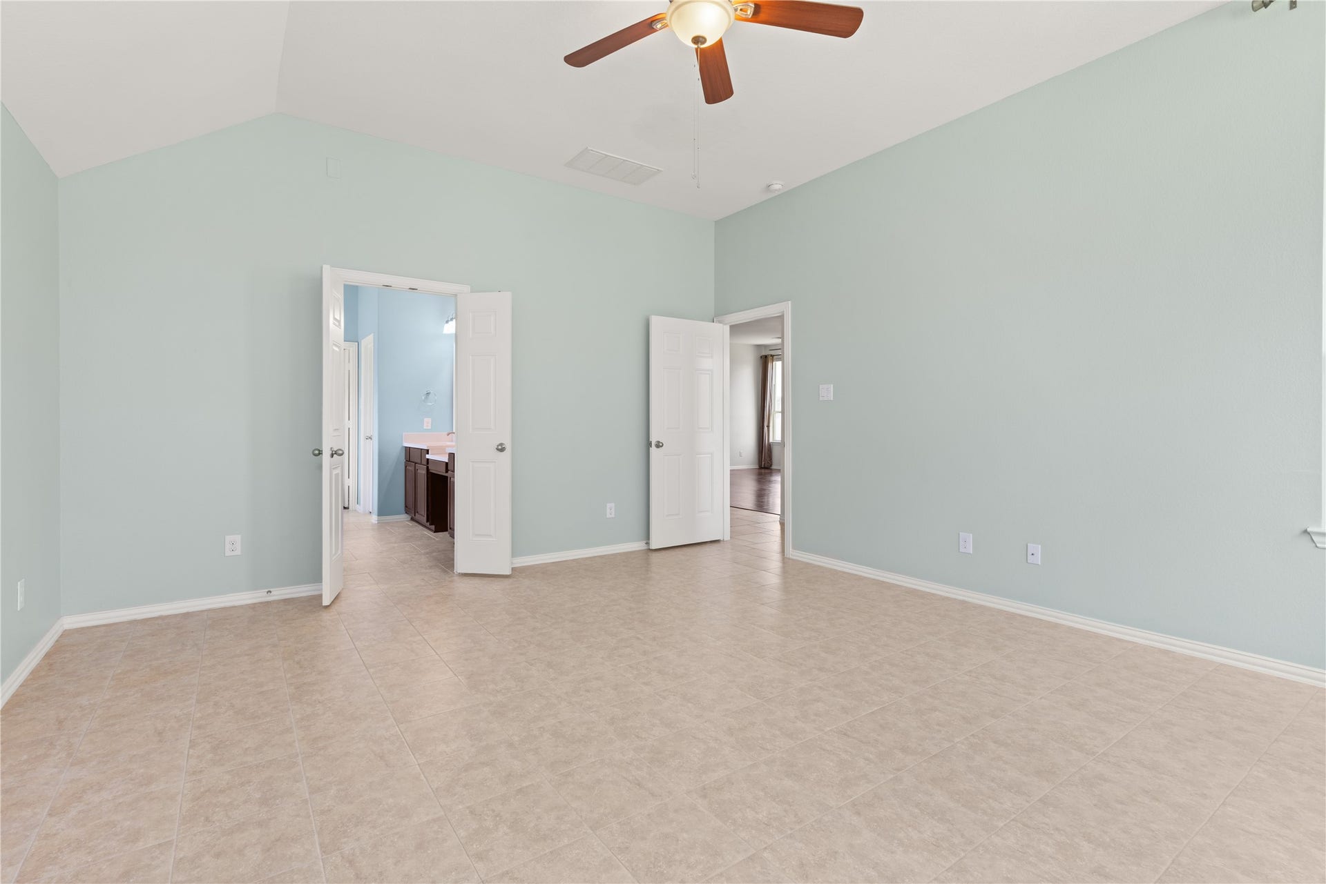 20507 Emery Manor Lane, Porter, TX 77365 Spacious bedroom with light-colored tile flooring, soft mint green walls, and a ceiling fan, leading to a bright ensuite bathroom and adjoining room.