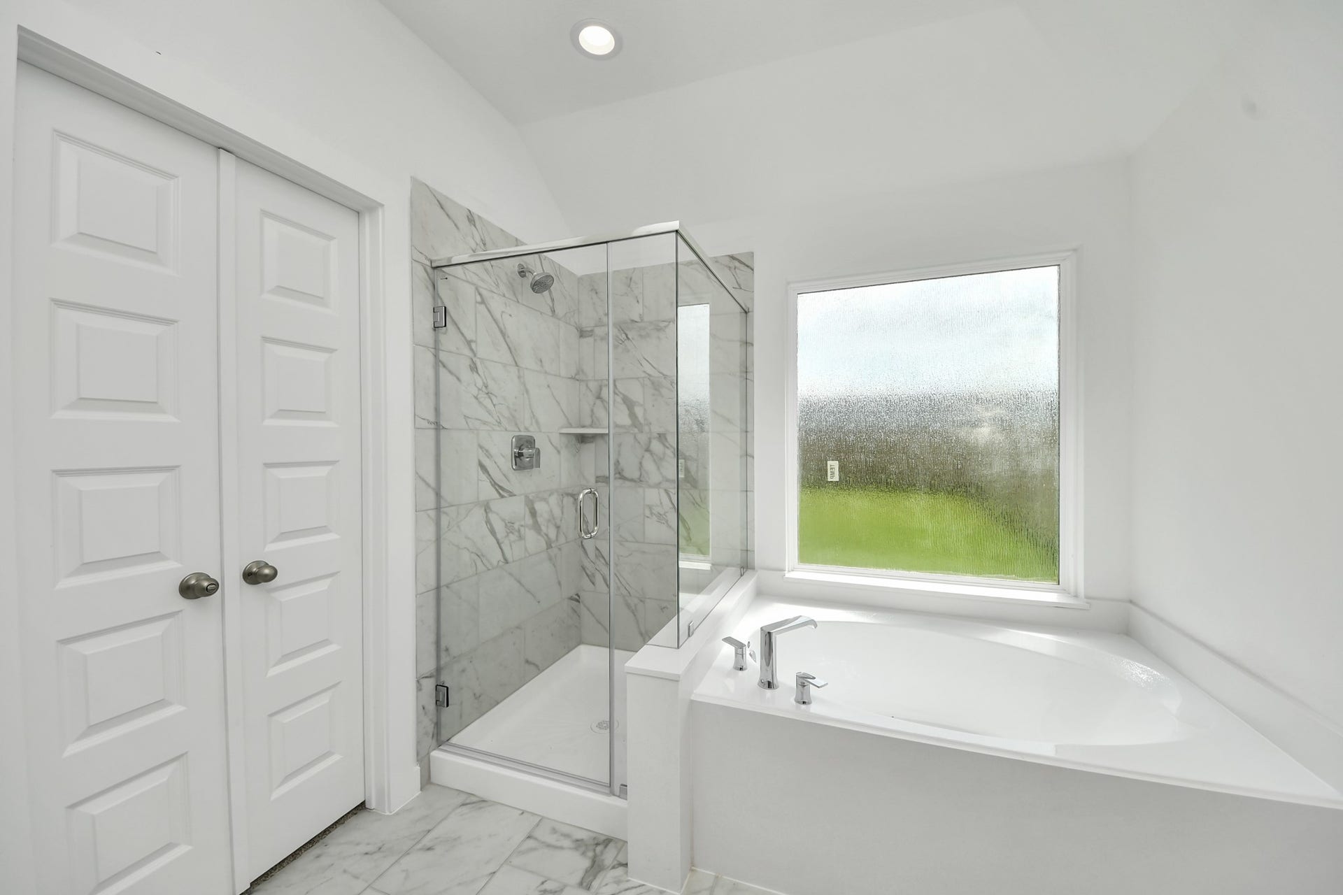 Escape to a spa-like oasis in this primary bathroom. Enjoy a walk-in shower with tile surround, a separate garden tub with custom detailing, and an elegant vanity featuring light countertops, modern hardware, and beautiful vanity lights. Experience luxury and relaxation in every detail. Sample photo of completed home with similar floor plan. Actual colors and selections may vary.