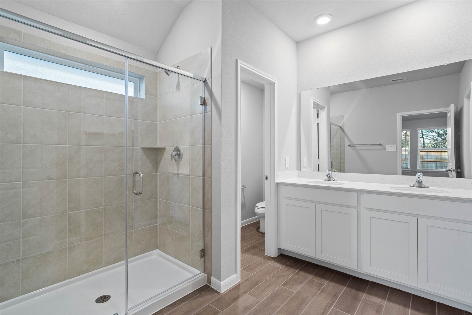19560 Stripe Hill Bend, Montgomery, TX 77316 A bright and functional primary bath offering dual sinks for busy mornings, a large mirror, and a modern glass-enclosed shower, creating a serene and efficient space.