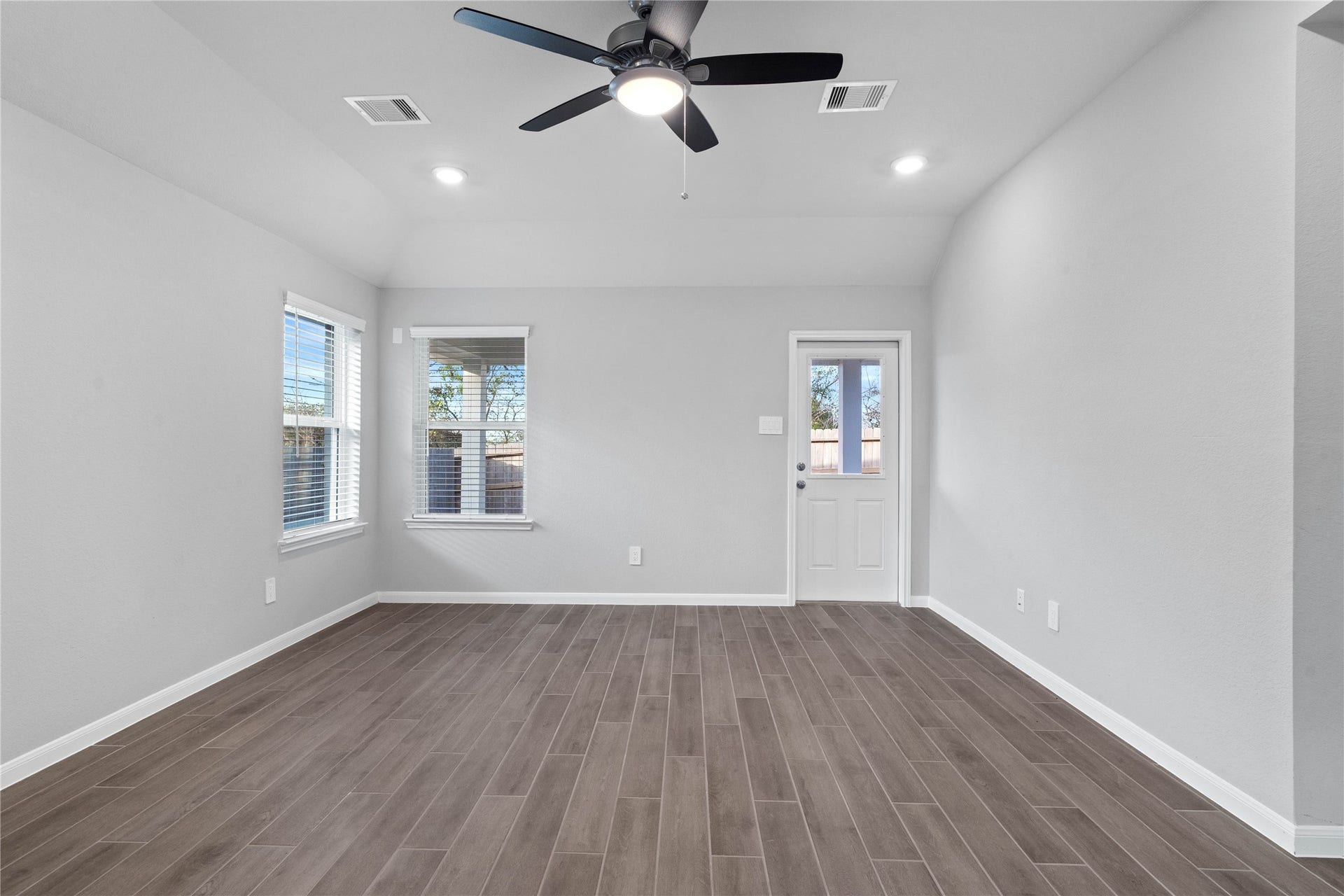 19560 Stripe Hill Bend, Montgomery, TX 77316 A bright and airy open-concept space featuring tile flooring, sloped ceilings with recessed lighting and ceiling fan, abundant natural light from large windows (fitted with blinds), and an access door to the back covered patio.