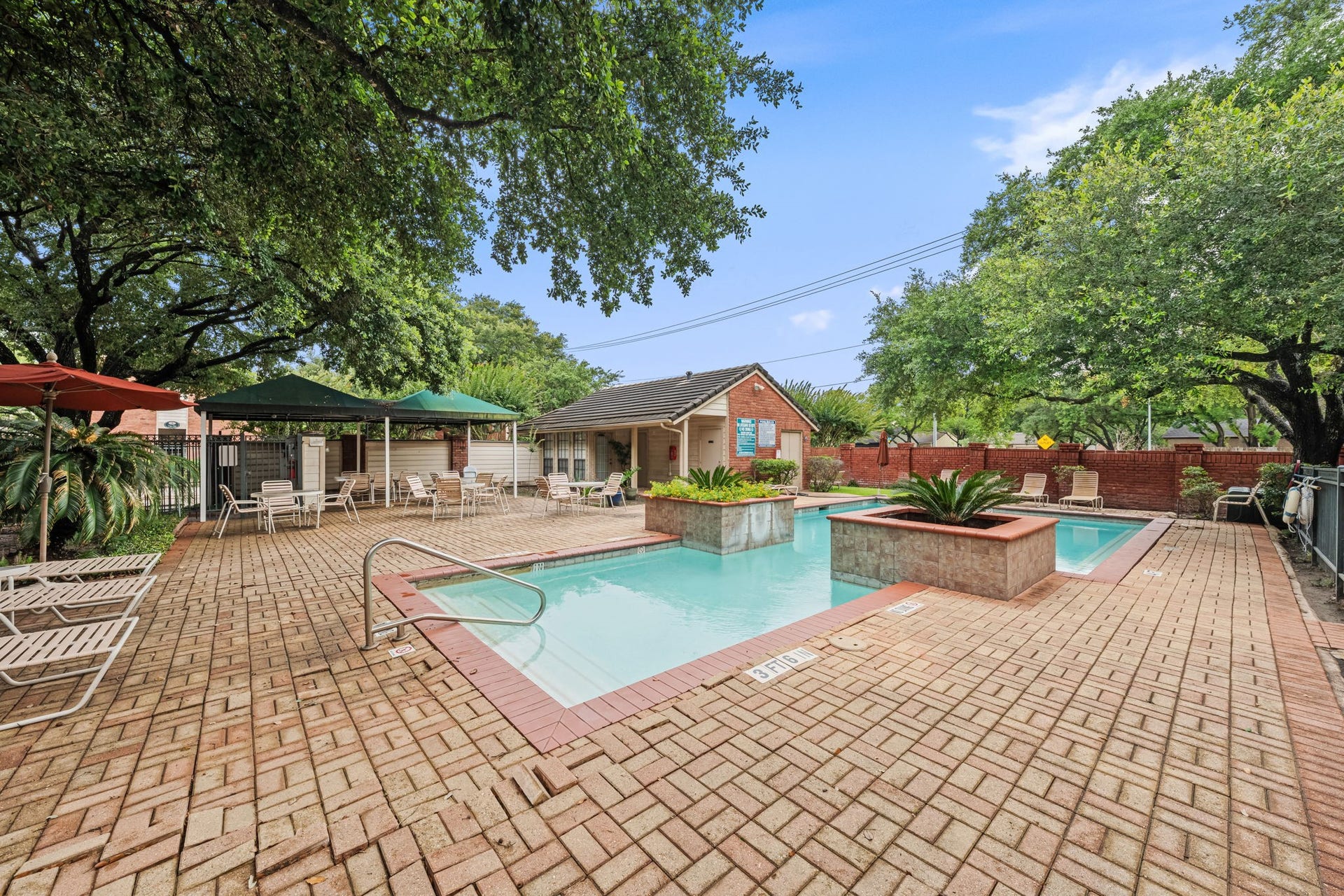 2211 S Kirkwood Road, #1, Houston, TX 77077 The wider view of the pool area reveals the full scope of the amenity a full brick paver surround with room to spread out, covered seating with shade umbrellas, and a mature oak canopy overhead that gives the entire space an established, private quality the photos don't fully capture at closer range.