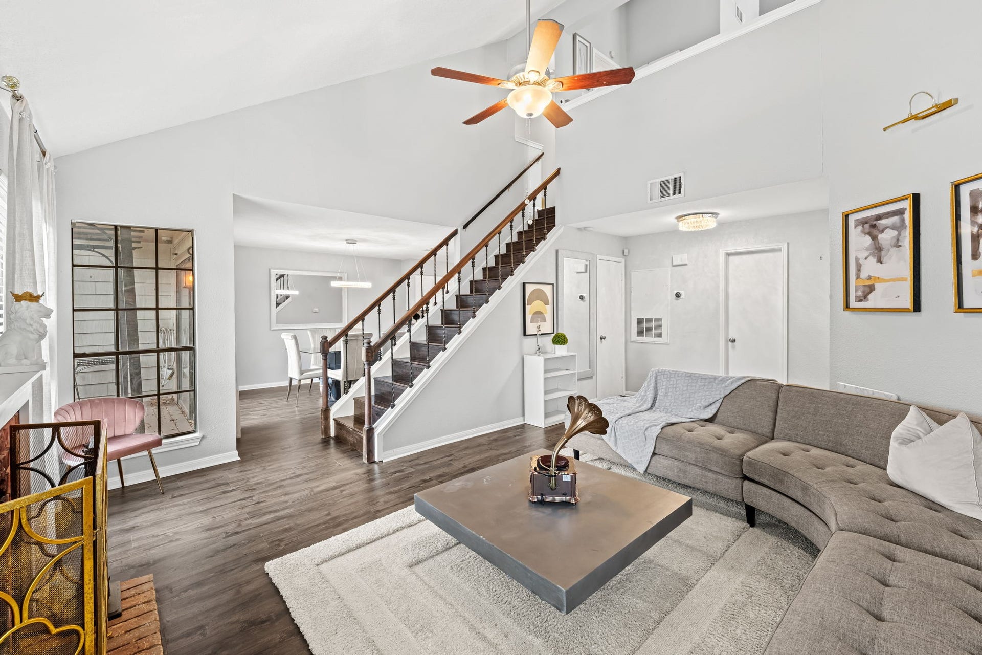 2211 S Kirkwood Road, #1, Houston, TX 77077 This wide view confirms what the first floor is actually delivering a vaulted ceiling spanning the full combined length of the living and dining areas, with the dark wood staircase rising at center and the dining room's crystal ring pendant visible in the distance. The entry door and front of the unit are visible at the far end, communicating the full depth and openness of the layout in a single frame.