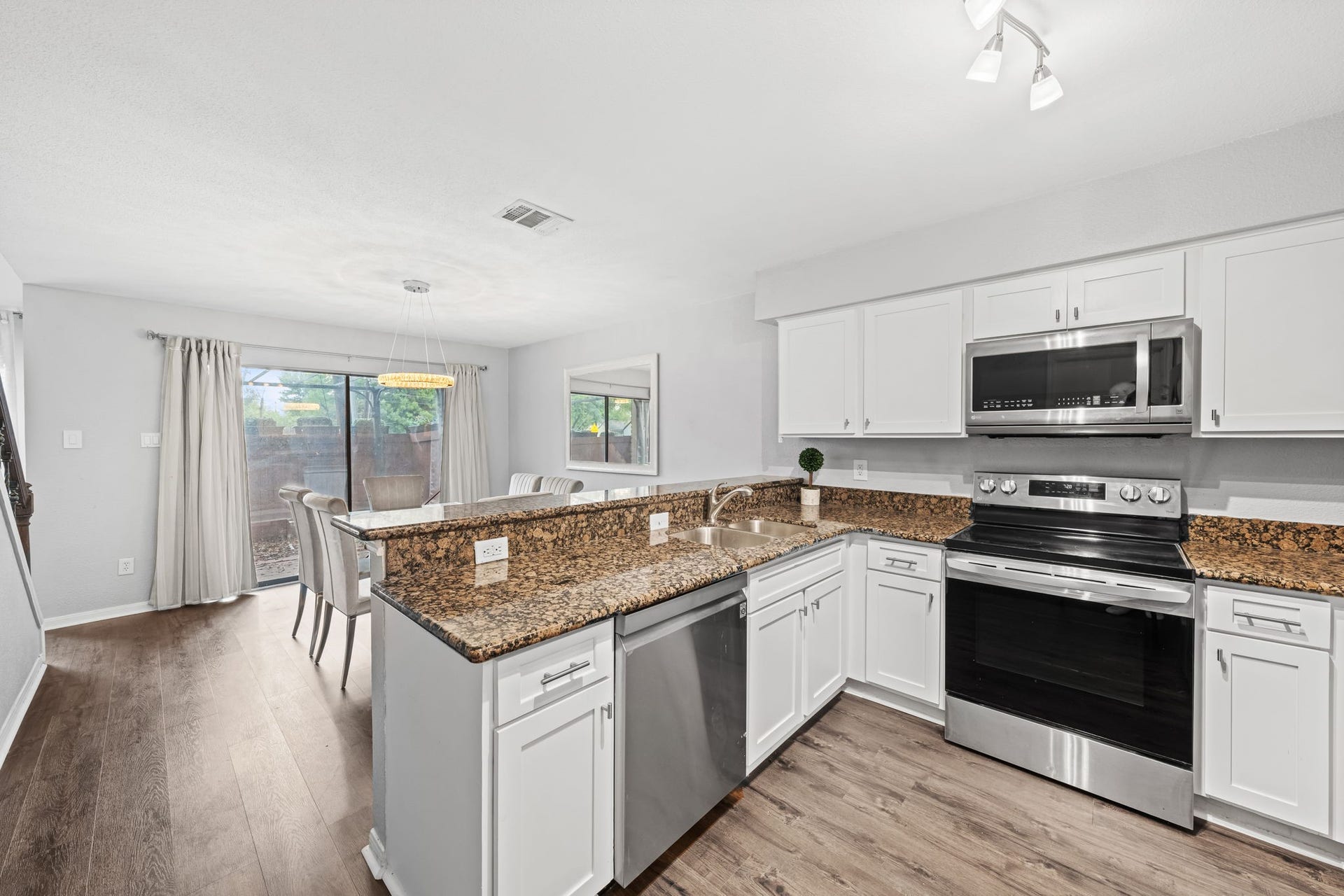 2211 S Kirkwood Road, #1, Houston, TX 77077 This kitchen is fully outfitted white shaker cabinetry with soft-close hardware runs the full perimeter, dark speckled granite countertops cover every surface including the breakfast bar peninsula, and the stainless steel appliance suite includes an electric range, dishwasher, over-range microwave, and a French door refrigerator with water and ice dispenser. The breakfast bar connects directly to the dining area, keeping the kitchen open to the rest of the first floor.