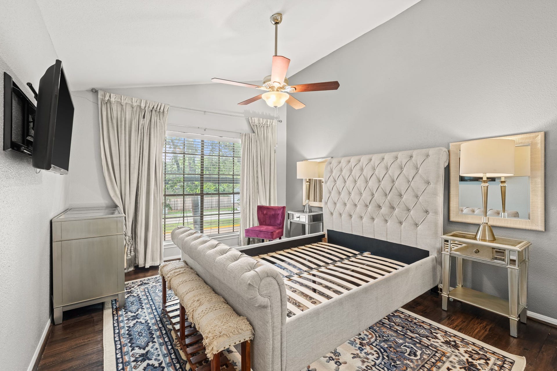 2211 S Kirkwood Road, #1, Houston, TX 77077 The primary bedroom carries the home's vaulted ceiling upstairs an angled plane rising to a ceiling fan at the apex gives the room a sense of height and openness that a standard second-floor bedroom simply doesn't have. The large exterior window brings in natural light and a view of the greenery outside.