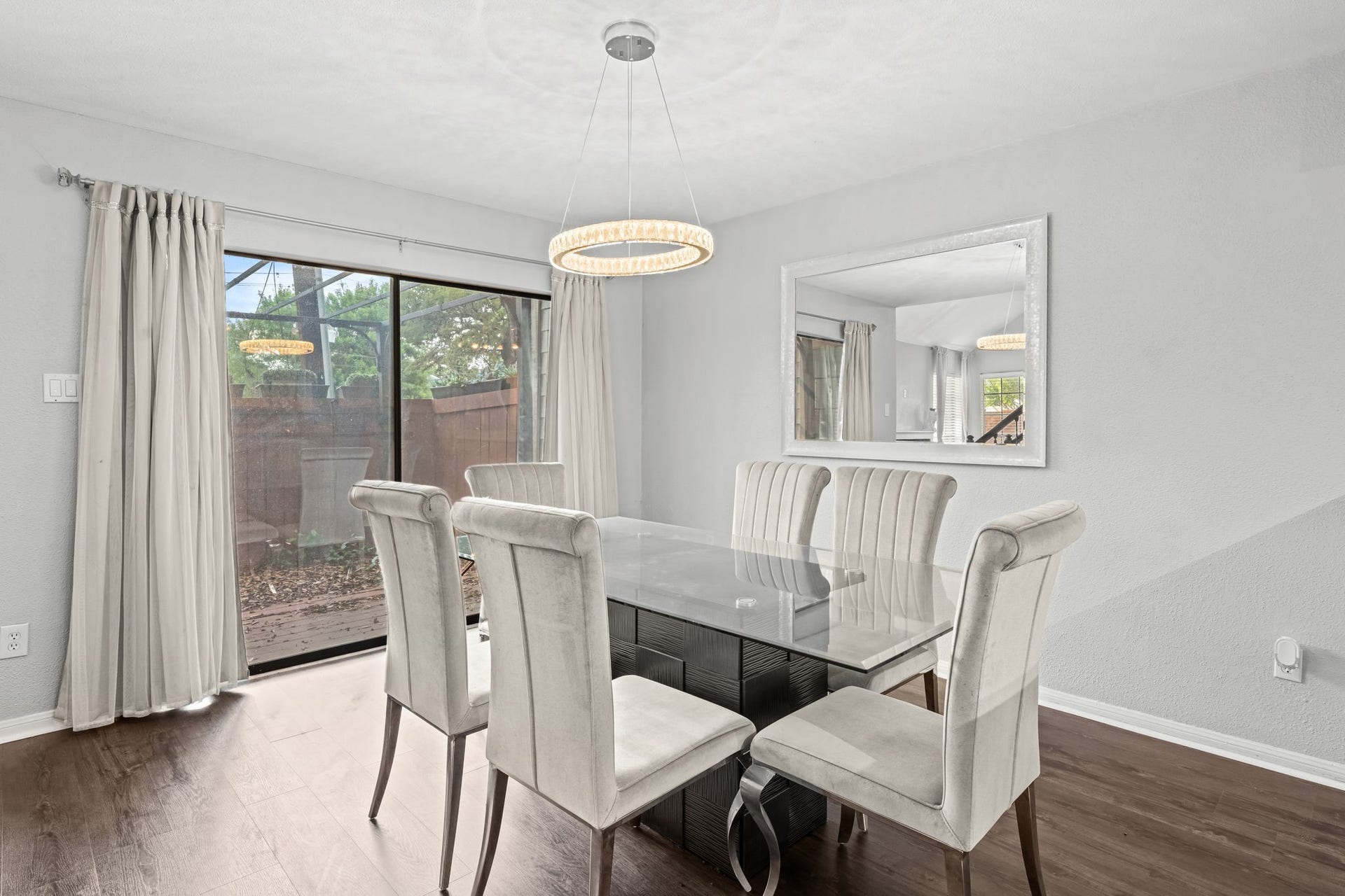 2211 S Kirkwood Road, #1, Houston, TX 77077 Sliding glass doors on the far wall open the dining room directly to the private patio natural light floods through from outside, and the mature greenery beyond gives the outdoor connection a genuine sense of privacy. The crystal ring pendant is centered above the full dining area, and the room proportions give the space room to breathe.