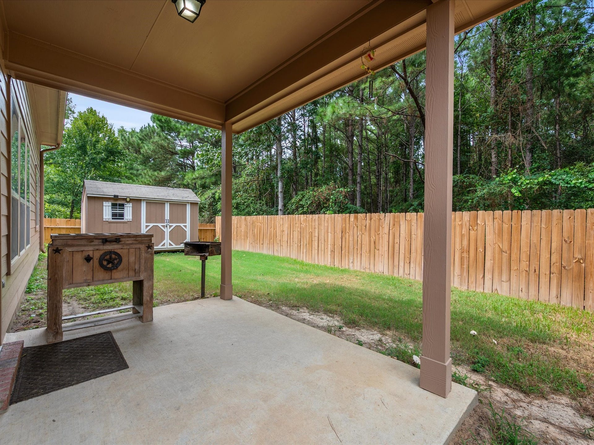 Covered patio opening to a private, fully fenced backyard with mature trees behind the property line, no rear neighbors, and a storage shed.