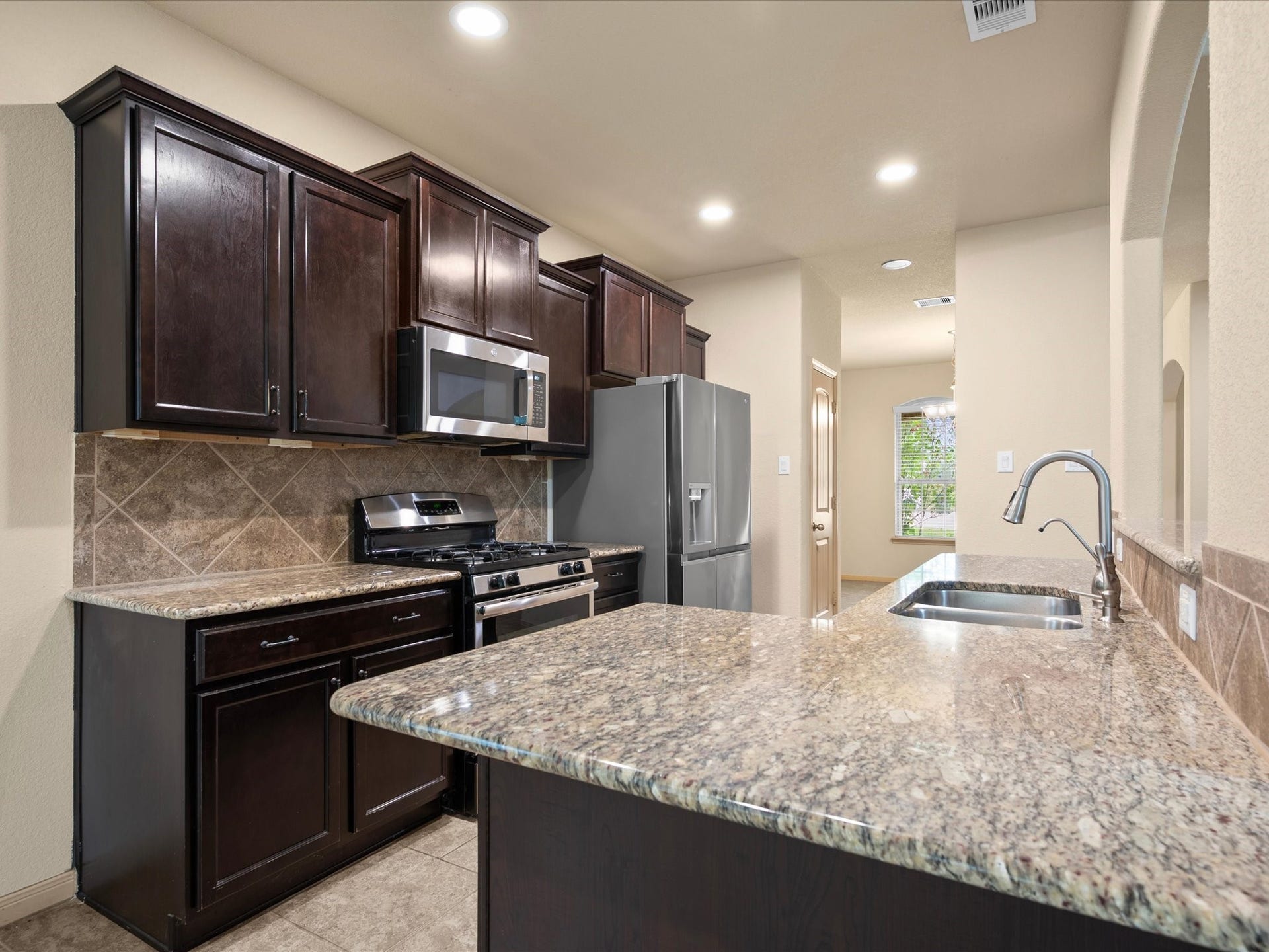 Functional kitchen showcasing rich espresso cabinetry, granite countertops, tile backsplash, and stainless steel appliances including a gas range and french door refrigerator.