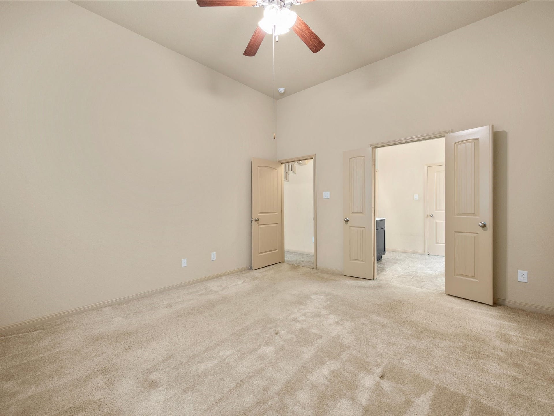 Primary bedroom view highlighting high ceilings, ceiling fan, plush carpet, and direct access to both the en-suite primary bath and large walk-in closet.