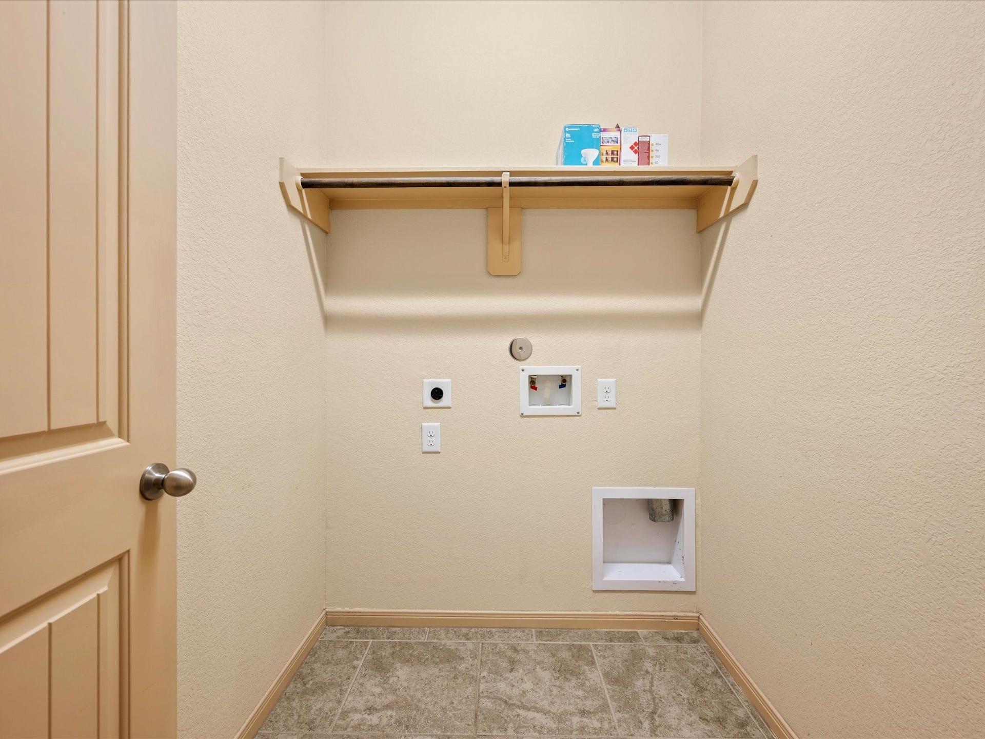 Dedicated laundry room featuring full hookups, durable tile flooring, and a built-in overhead shelf with hanging rod for added storage and utility.