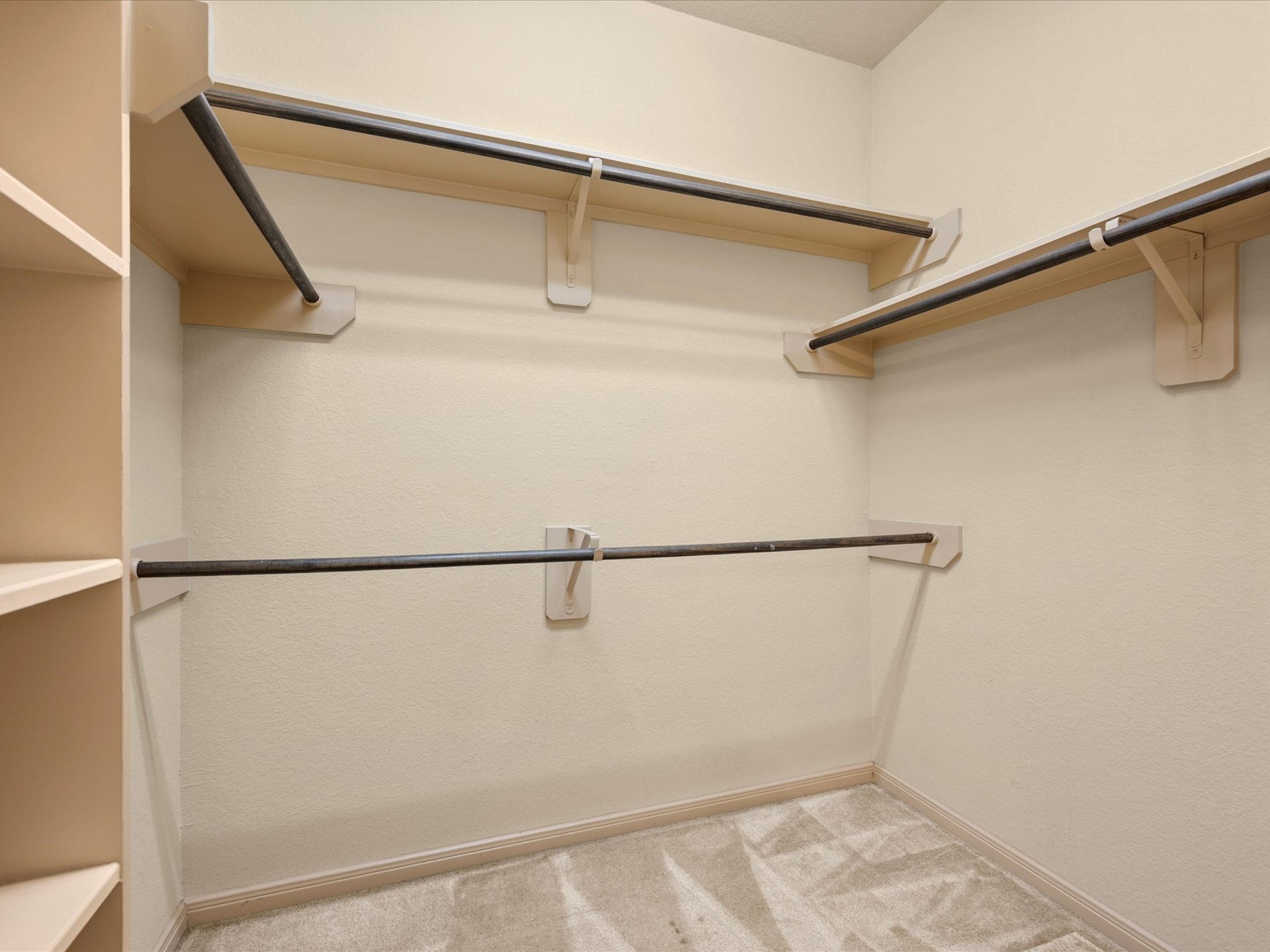 Generously sized primary walk-in closet outfitted with built-in storage solutions. Features multi-level hanging rods to maximize vertical space, upper shelving for folded items or storage bins, built-in cubbies/shelving, and soft carpet flooring.