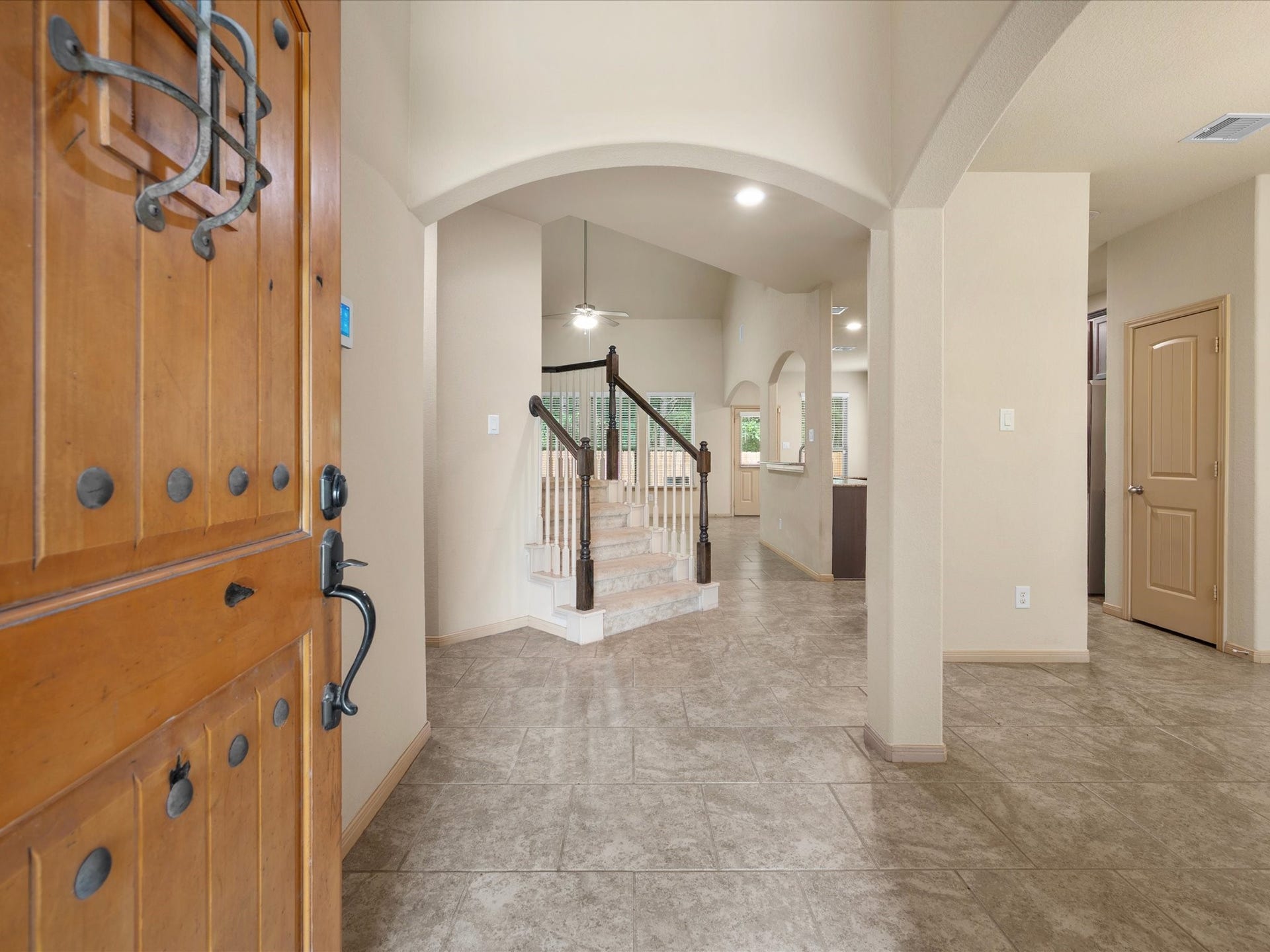 Welcoming entryway opening into a bright foyer with tile flooring, soft neutral paint, and decorative archways. Highlights a view directly to the staircase, high ceilings, and seamless flow into the main living areas.