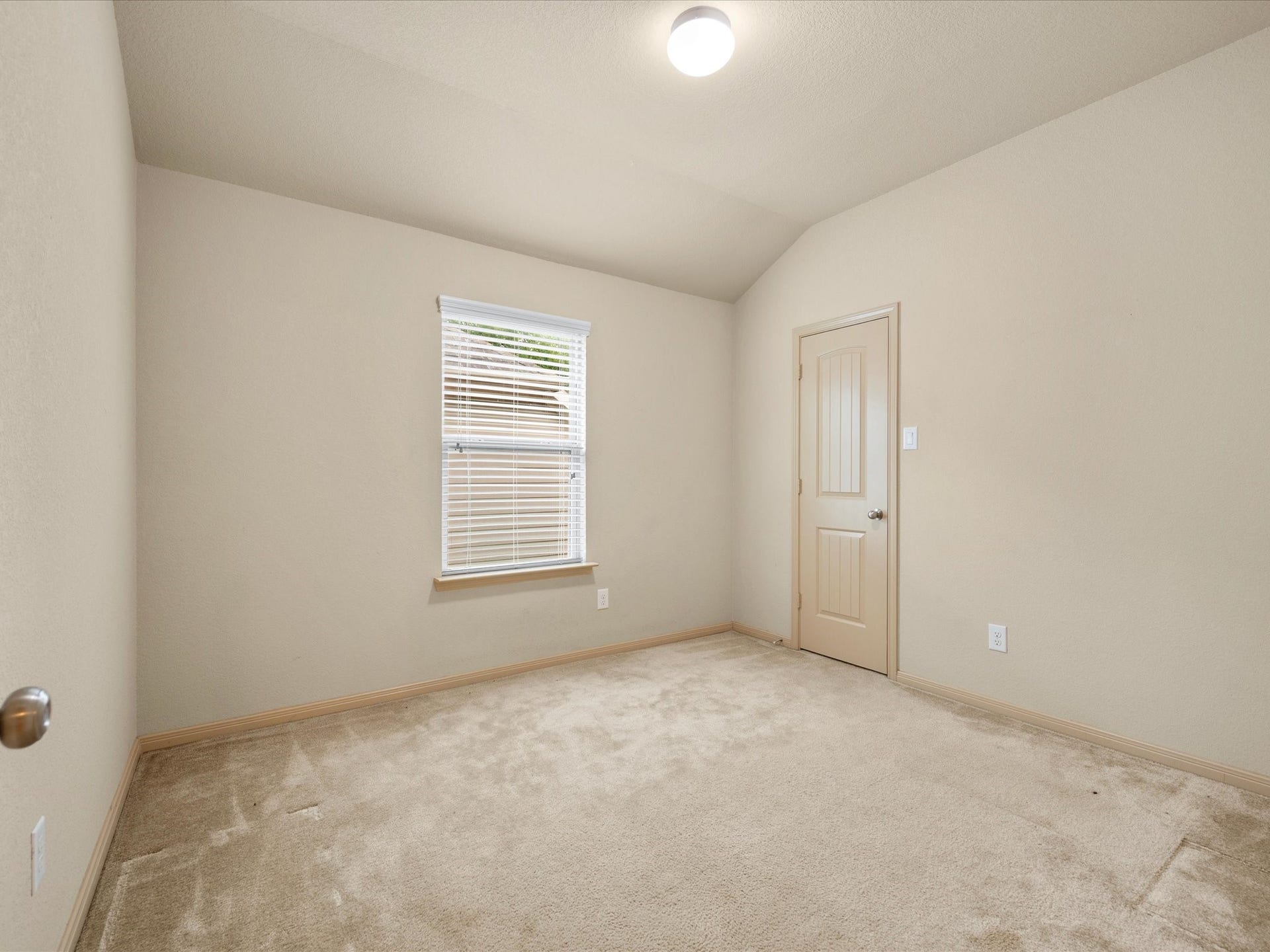 Secondary bedroom featuring plush carpeting, a vaulted tray ceiling, neutral finishes, and natural light, ready to be tailored as a guest room or home office.