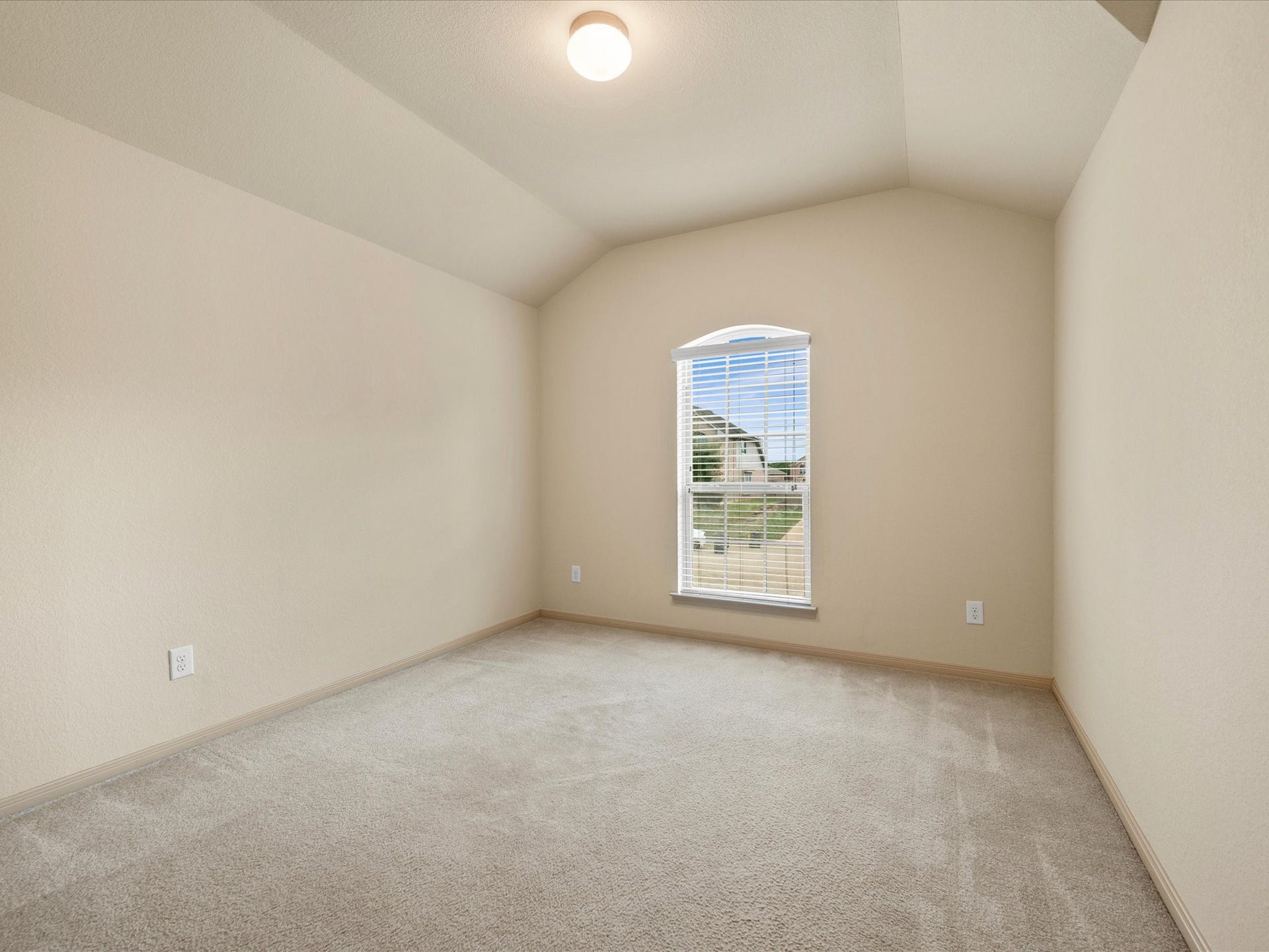 Secondary bedroom featuring dramatic vaulted ceilings, plush carpeting, neutral finishes, and a focal arched window providing abundant natural light.