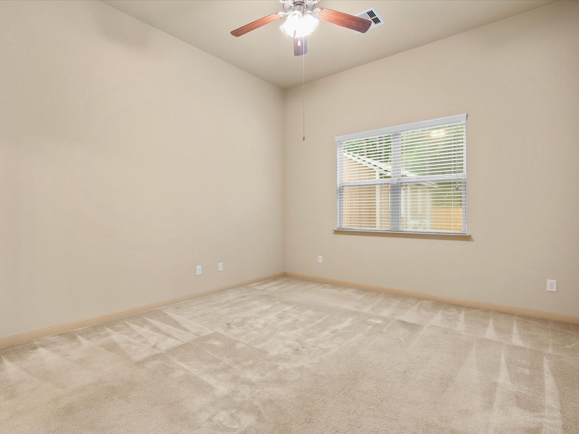 Generously sized primary suite featuring high ceilings, plush carpeting, a central ceiling fan, and natural light. Offers plenty of room for a complete bedroom suite.