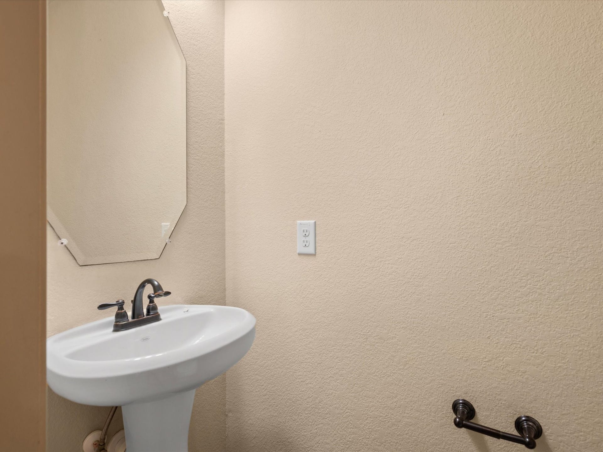 Convenient main-level powder room perfect for guests. Features a classic white pedestal sink paired with a stylish bevel-edged wall mirror, and clean, neutral wall finishes.