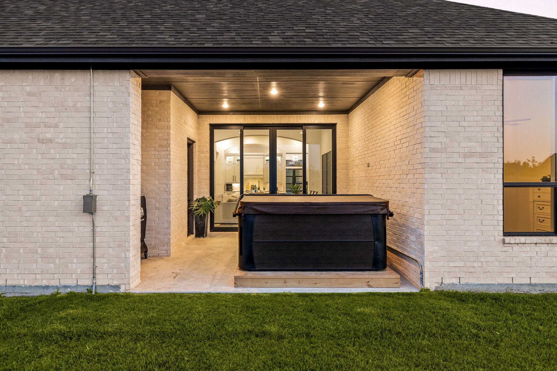 31322 Crescent Hill Drive, Fulshear, TX 77441 An inviting outdoor living space. This covered backyard patio features clean light brick columns, dark gutters, recessed ceiling lighting, a concrete floor, and glass slider doors that create a seamless indoor-outdoor transition.