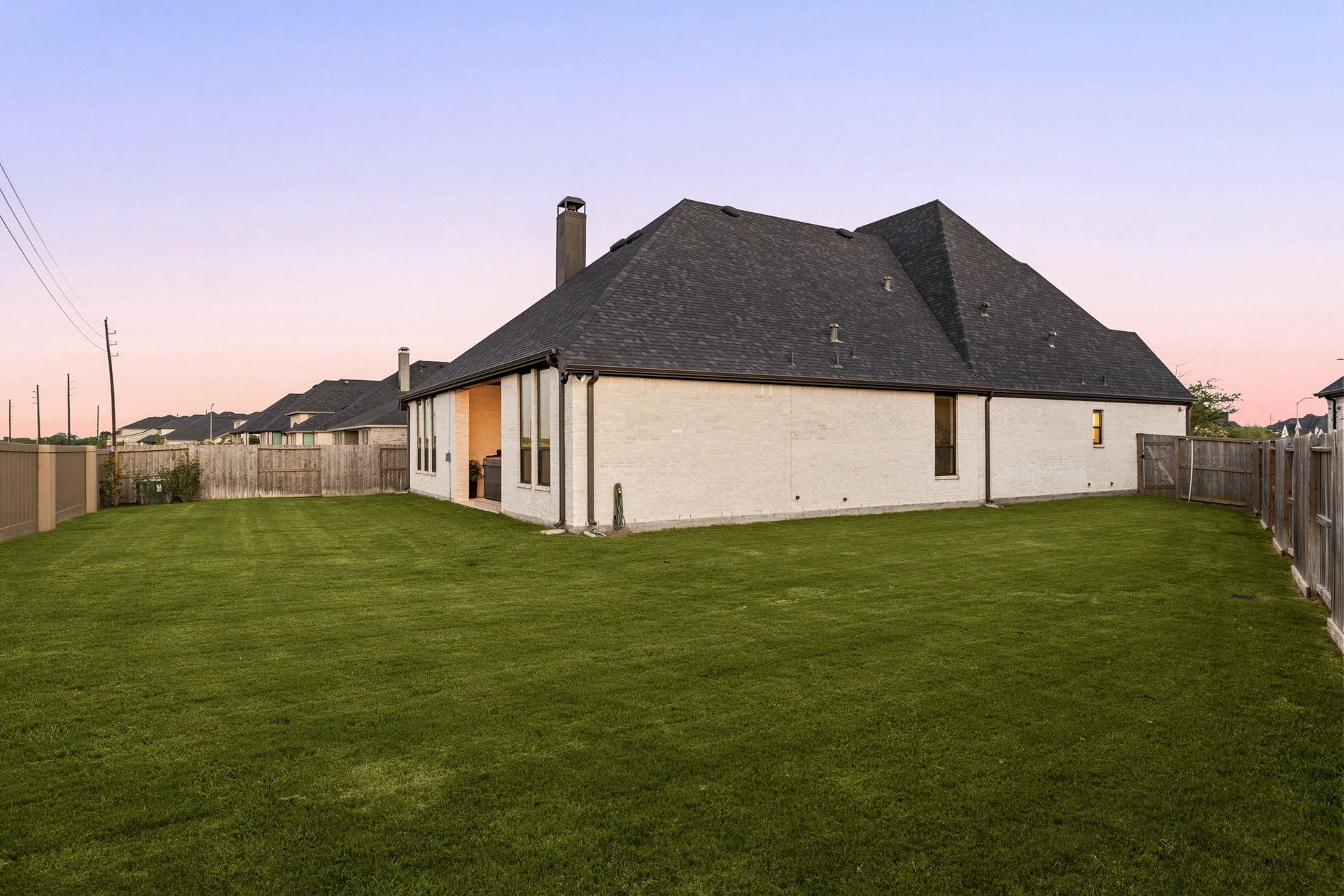 31322 Crescent Hill Drive, Fulshear, TX 77441 A pristine, low-maintenance exterior profile. This side view showcases the home's crisp light brick facade, clean rooflines, a continuous wooden privacy fence, and an expansive grassy lawn offering plenty of space for outdoor recreation.