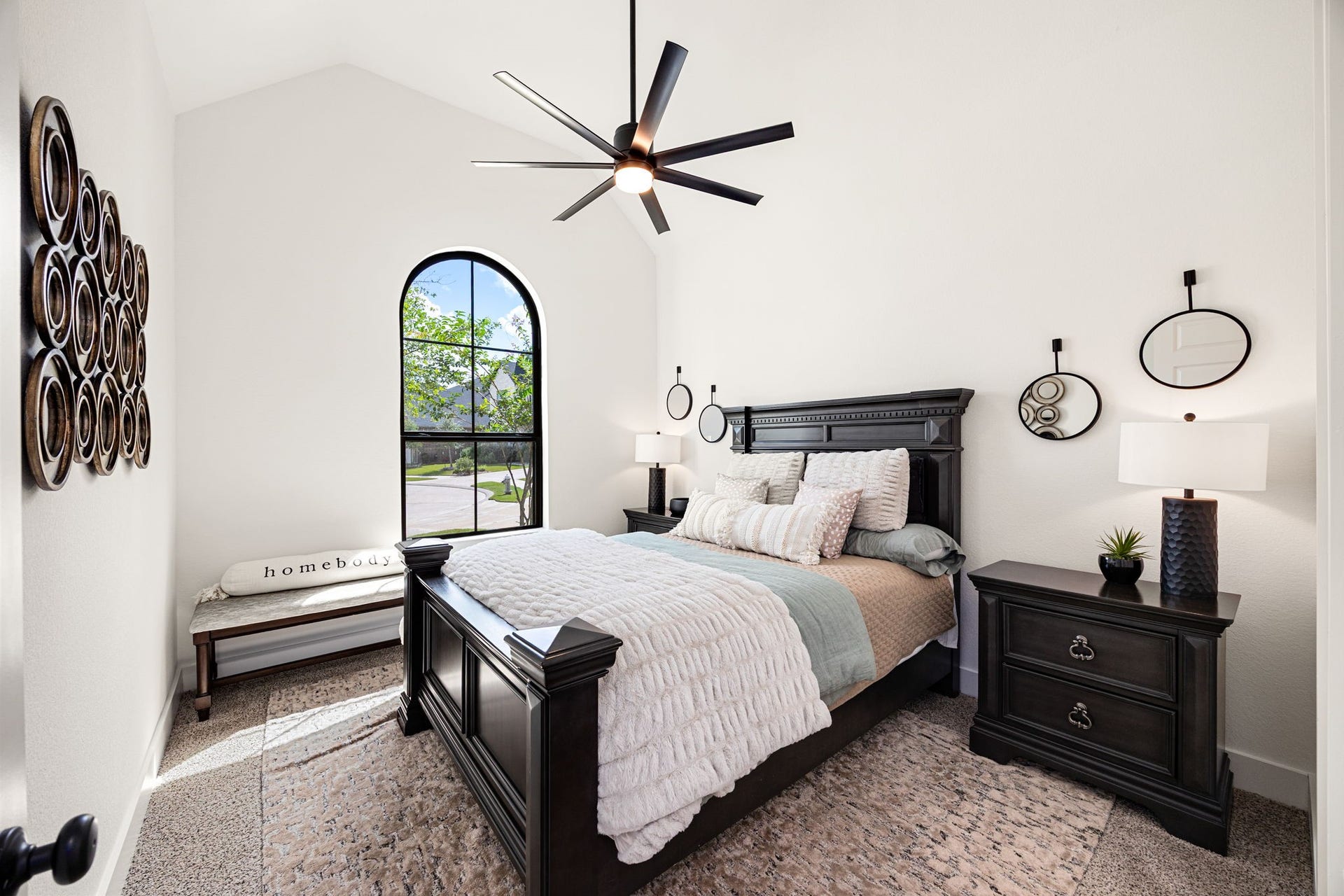 31322 Crescent Hill Drive, Fulshear, TX 77441 A charming and bright guest suite. A beautiful black-trimmed arched window anchors this inviting bedroom, highlighting plush neutral carpeting, soaring vaulted ceilings, a modern multi-blade ceiling fan, and clean matte black door hardware.