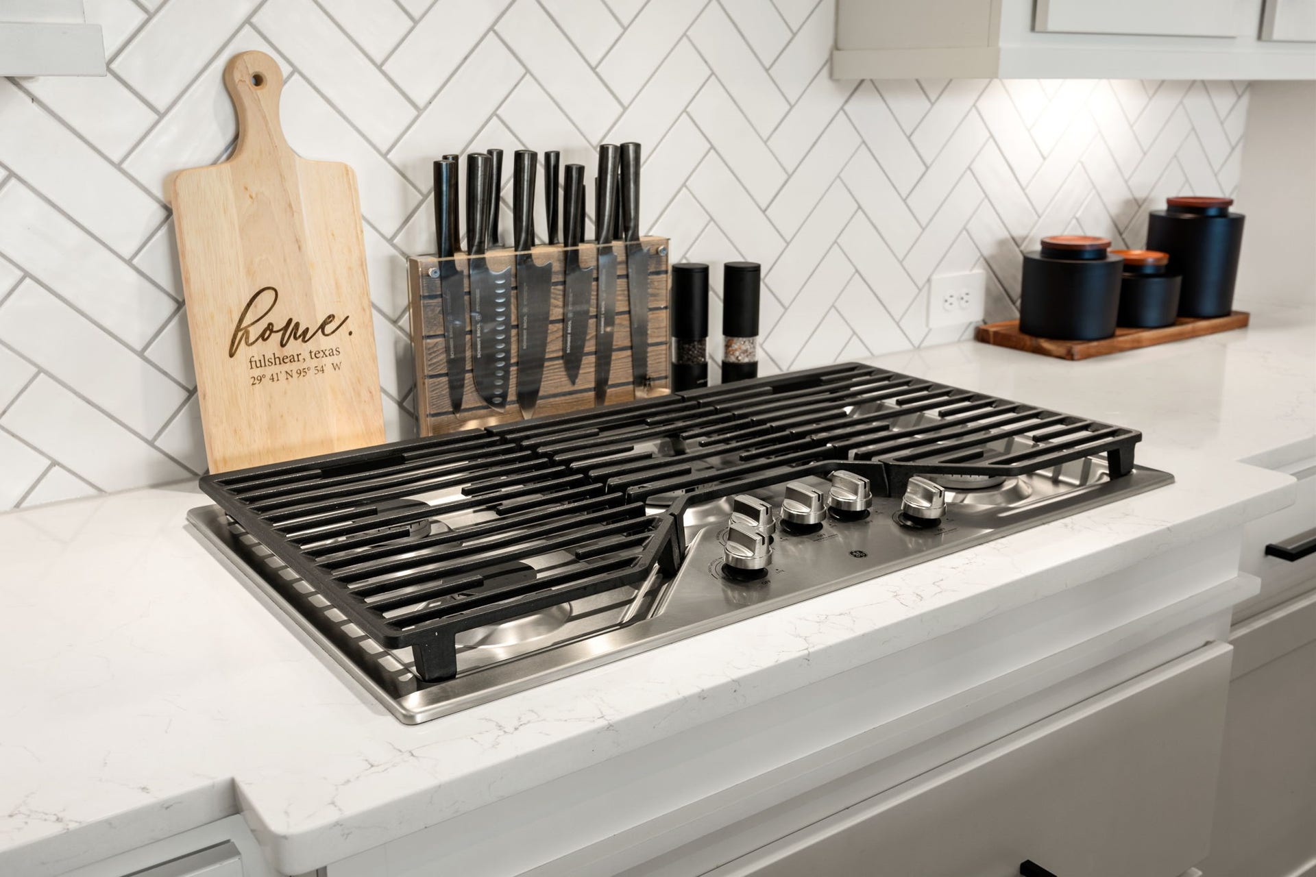 31322 Crescent Hill Drive, Fulshear, TX 77441 Premium culinary details. This chef-inspired cooking station showcases a high-end stainless steel gas cooktop with heavy-duty cast-iron grates, nestled into pristine white quartz countertops and framed by a classic white herringbone tile backsplash.